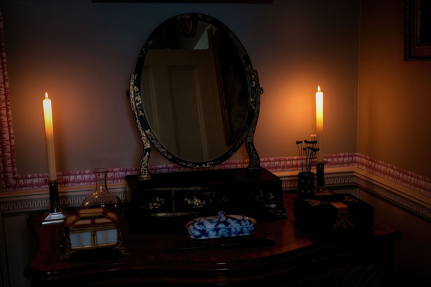 A row of glowing candles in dark glass holders creates a warm, atmospheric ambiance in a dimly lit room.