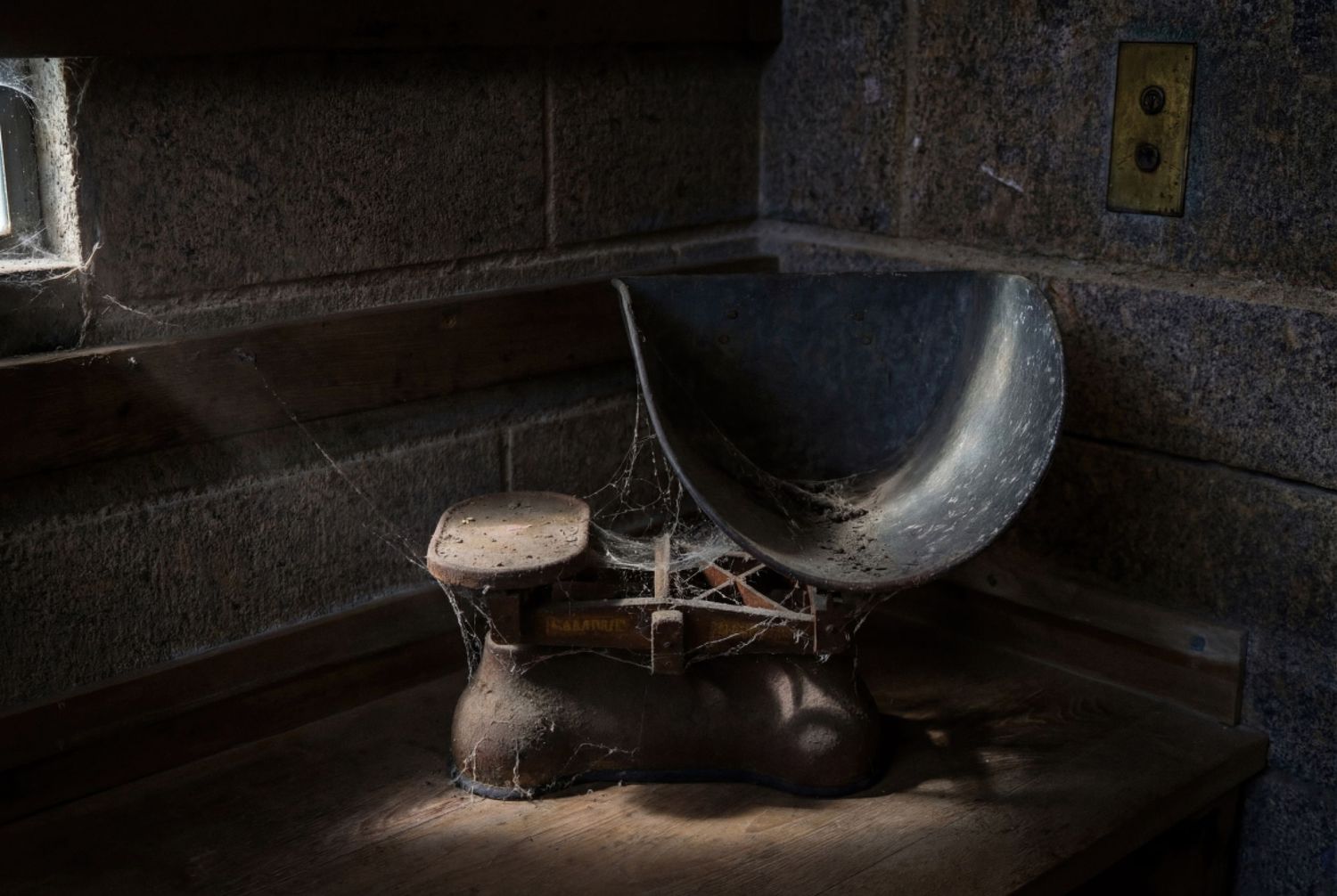 Vintage rustic balance scale with metal scoop sits in dark corner of stone kitchen counter.