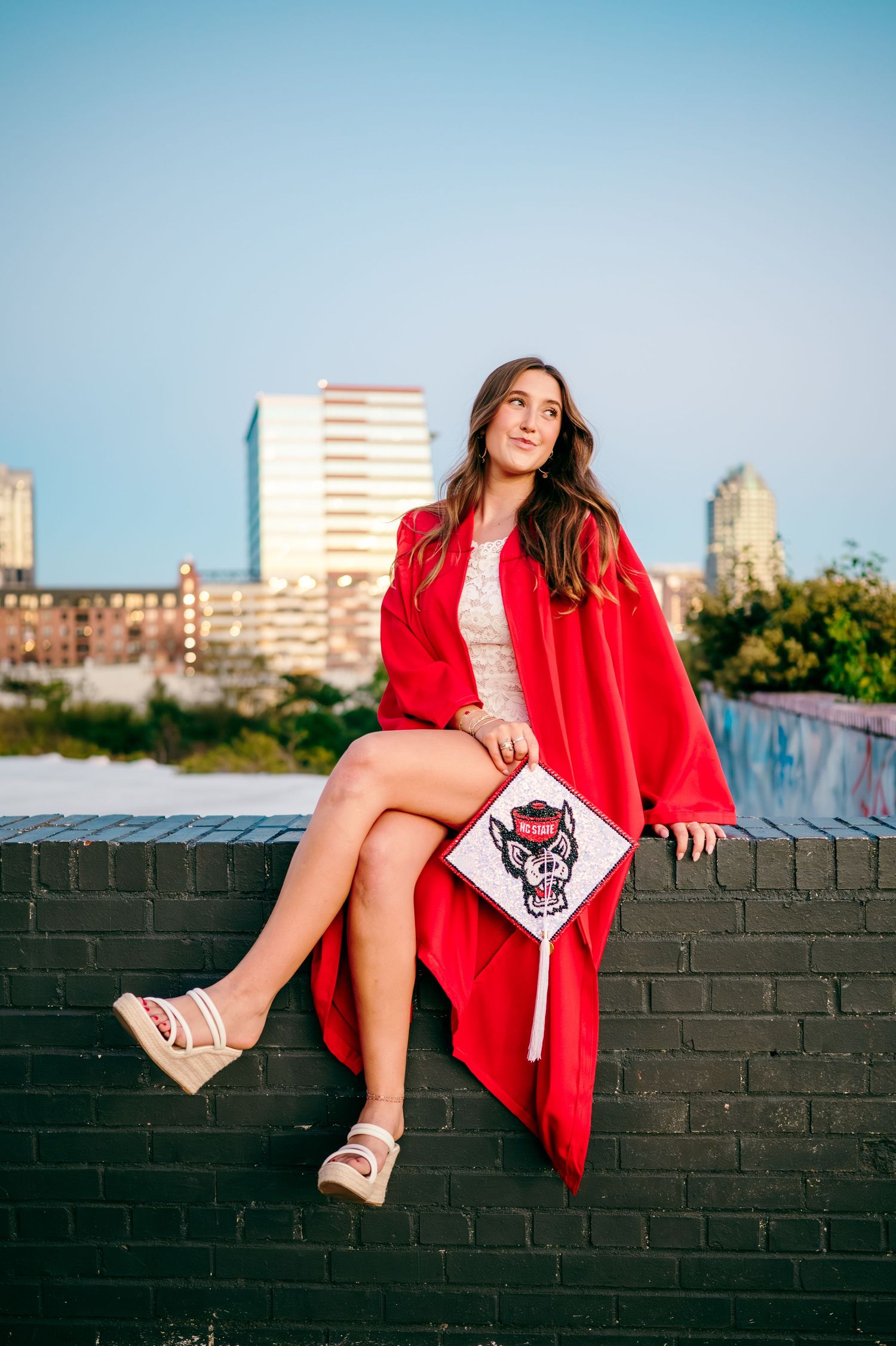 Cap and gown grad photos with the Raleigh skyline in the background at boylan bridge