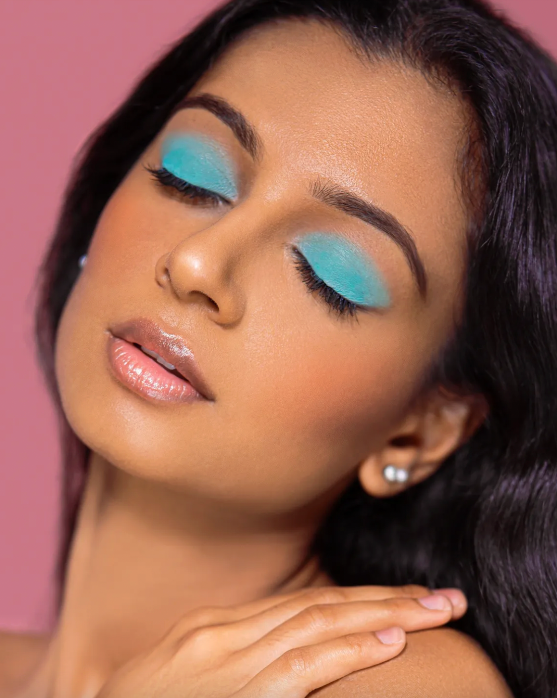 Closeup beauty portraits featuring turquoise eyeshadow and glowing skin against pink background.