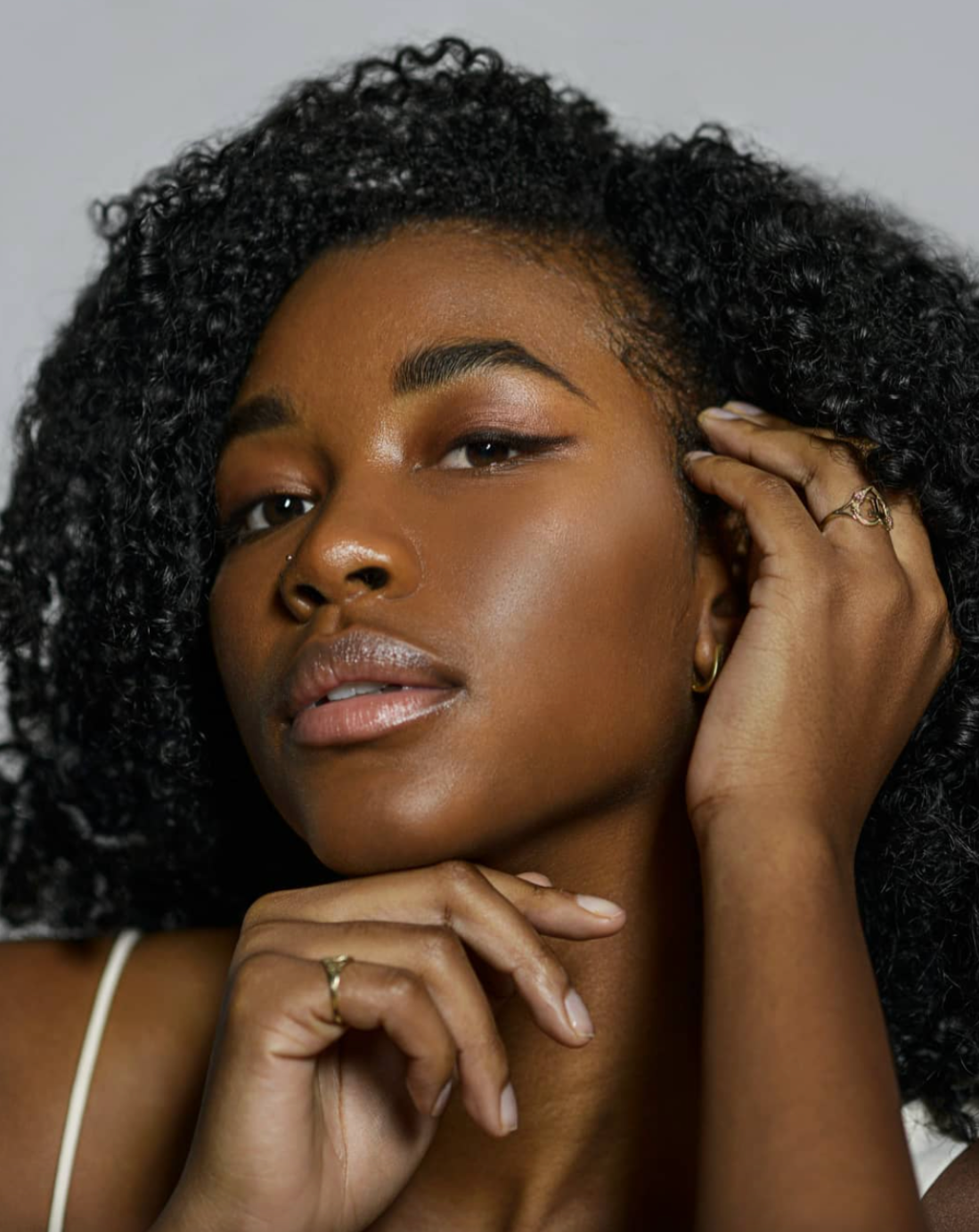 Artistic beauty shots highlighting natural curls and glowing skin against gray backdrop.