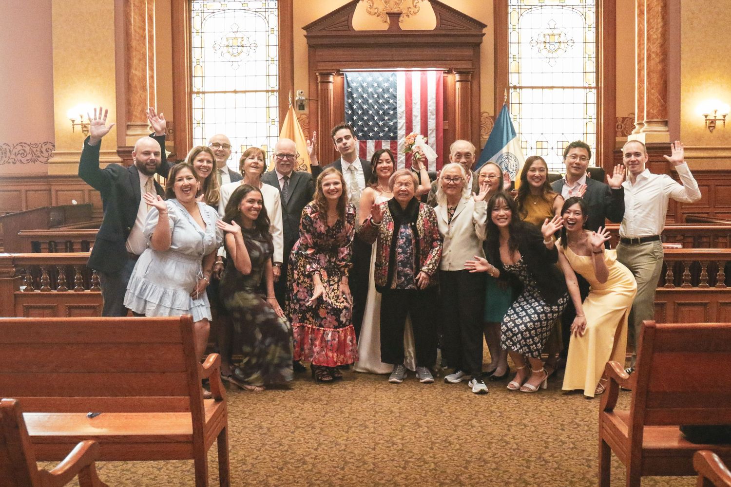 Large group celebrating in a courtroom with American flag, posing joyfully after a ceremony.