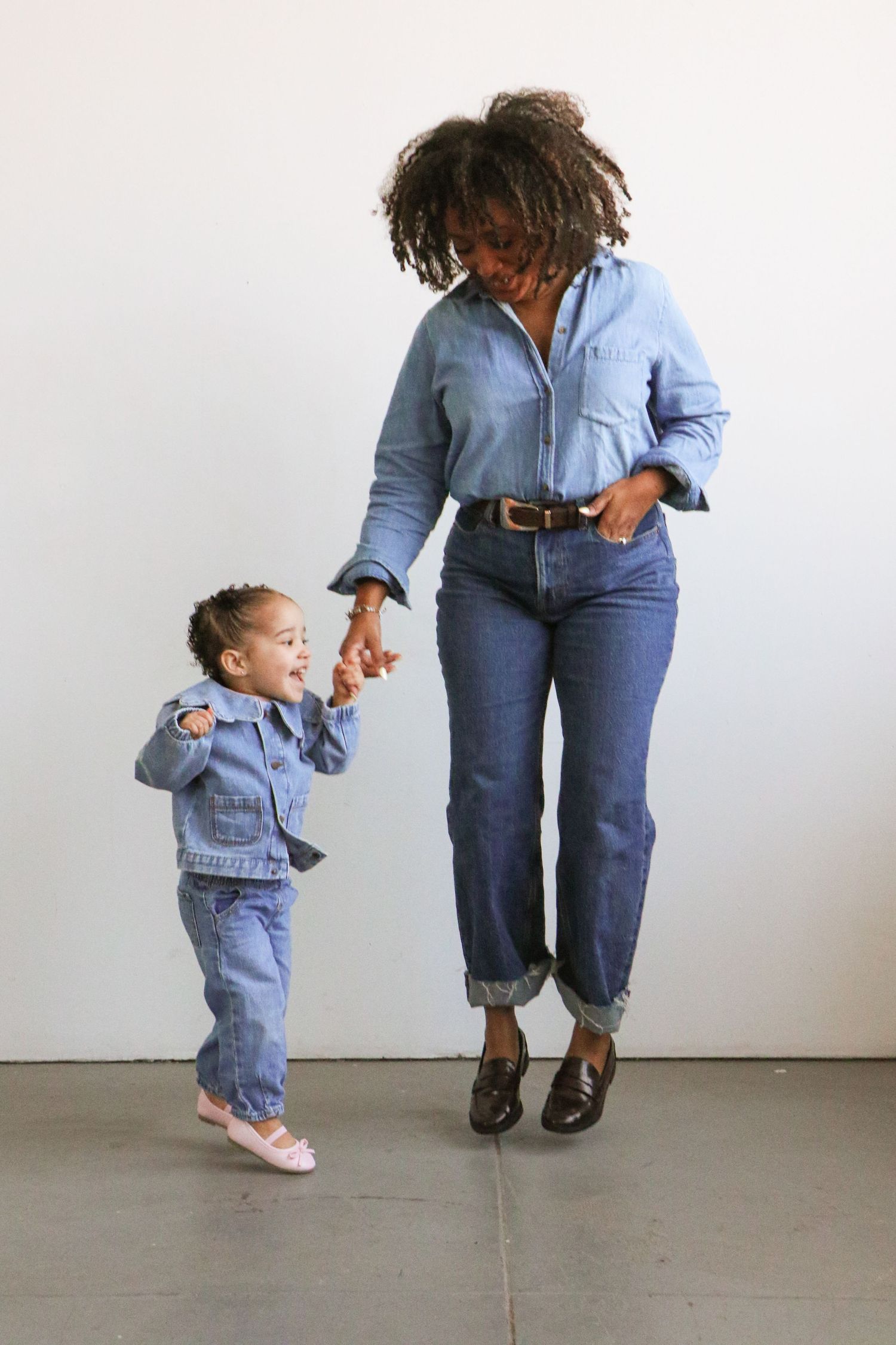 Black mother in denim shirt and jeans dancing with toddler daughter in denim outfit.