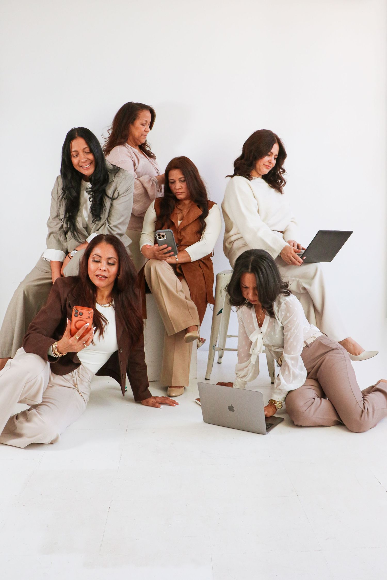 Group of six diverse women posing with laptops and phones on white background.