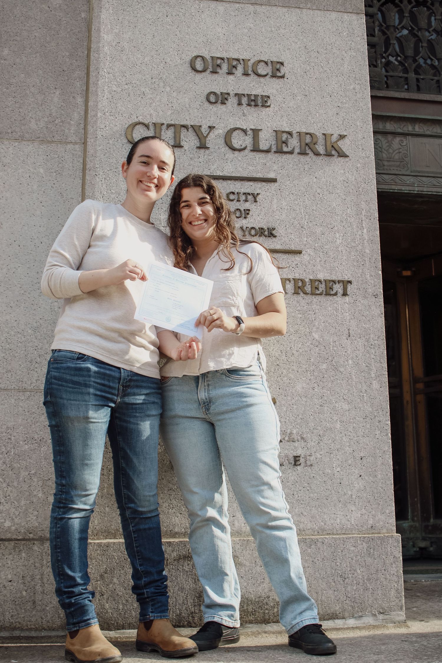 Two women proudly holding a document outside the Office of the City Clerk in New York City.