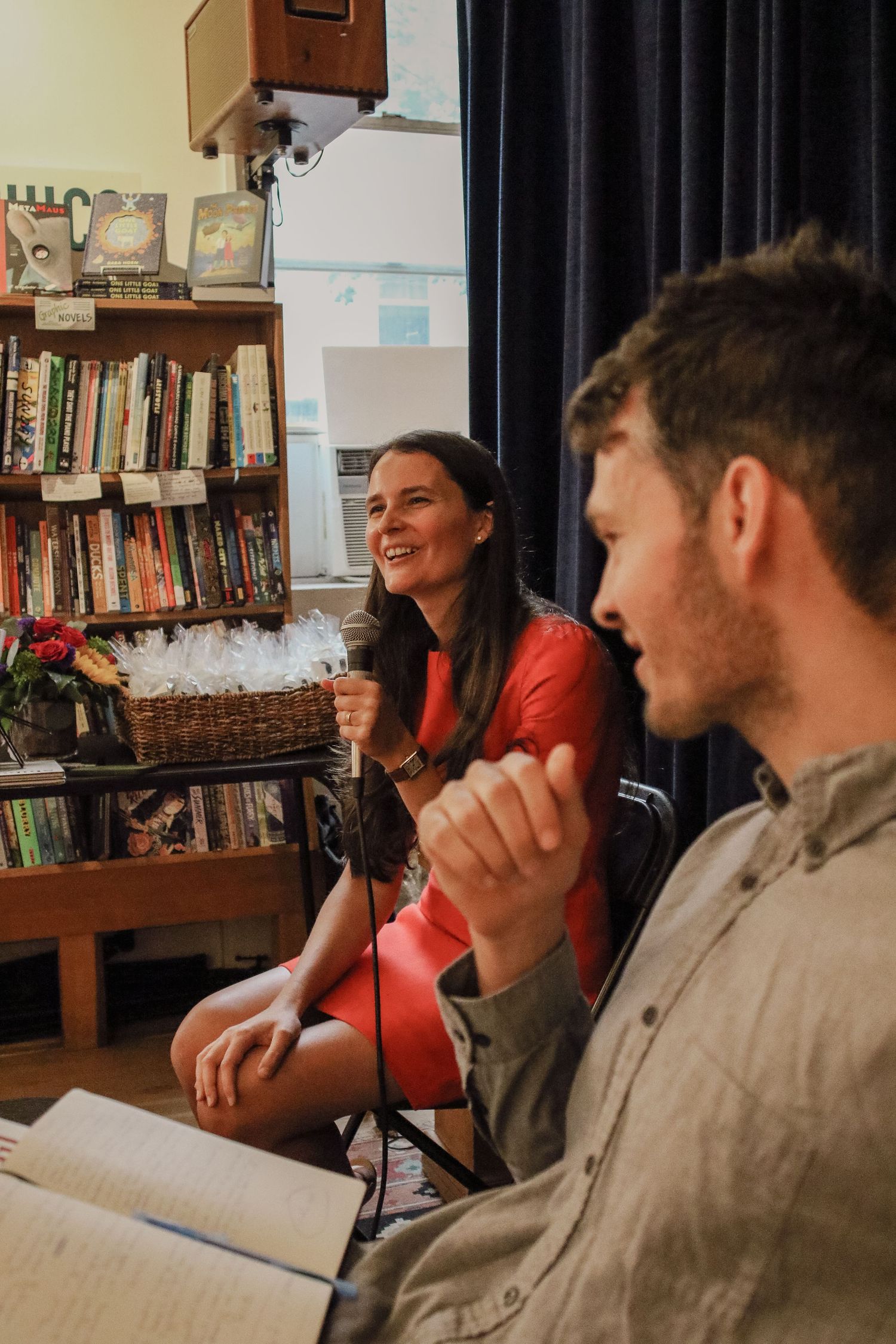 Woman in red dress laughing while holding microphone at a bookstore panel discussion.
