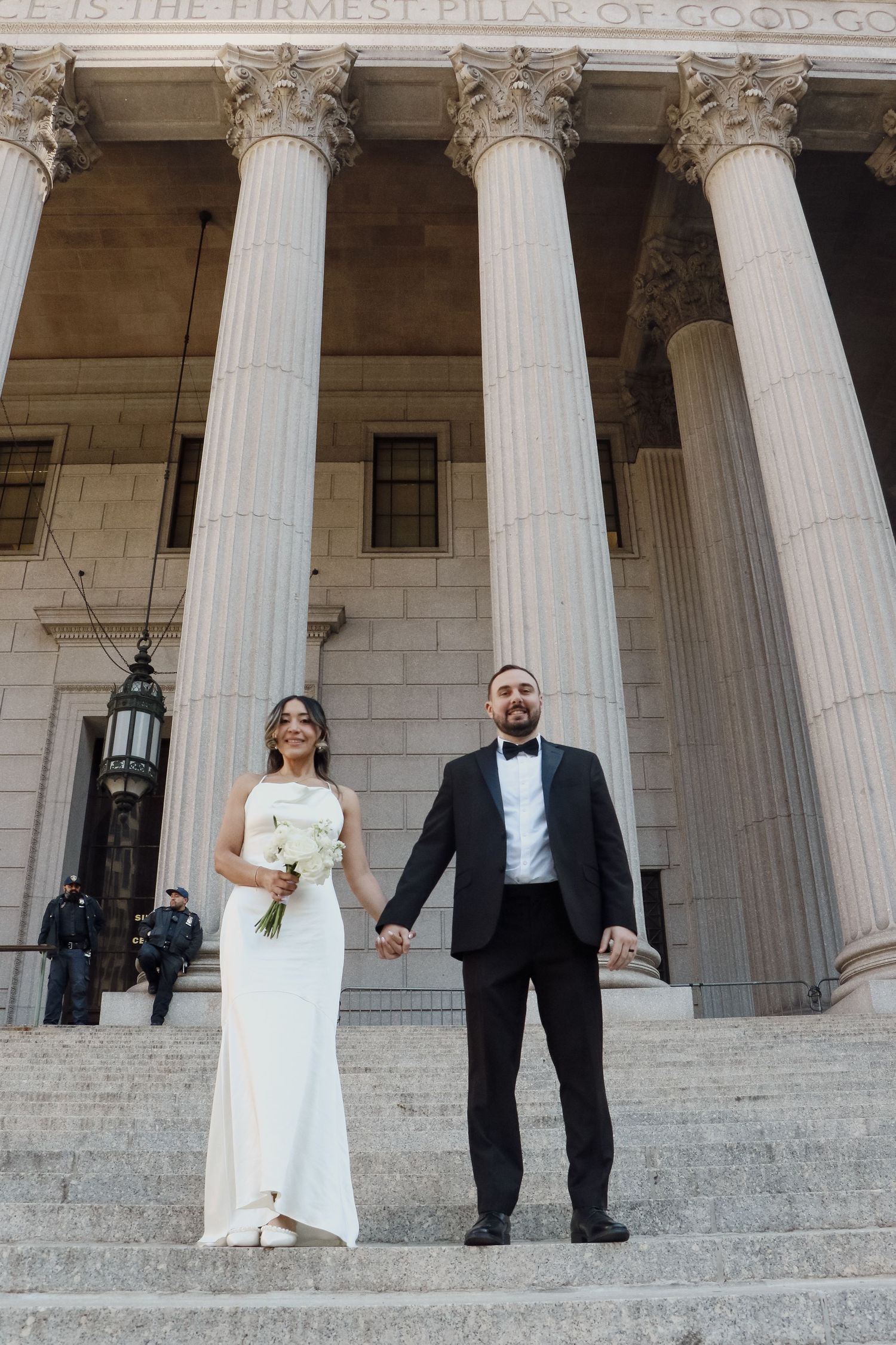 Bride and groom hold hands on steps of grand NYC courthouse with towering Corinthian columns.