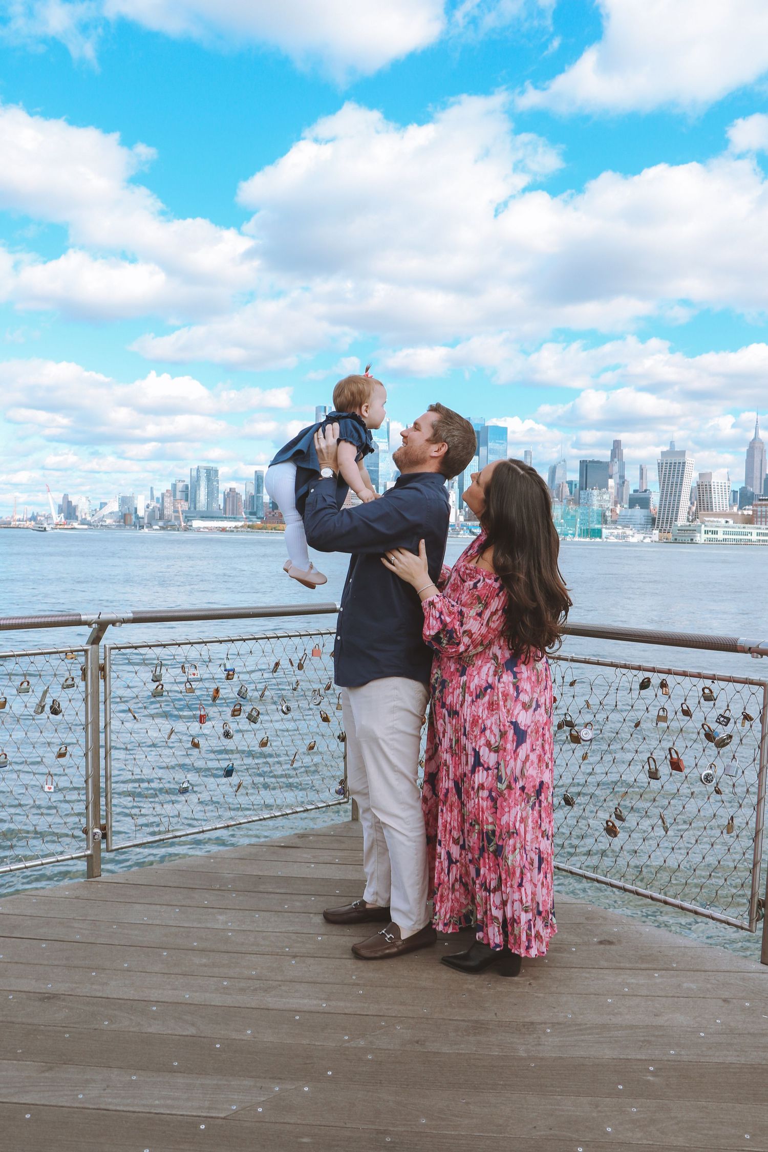 Family portrait with baby on NYC waterfront pier with Manhattan skyline and love locks on railing.
