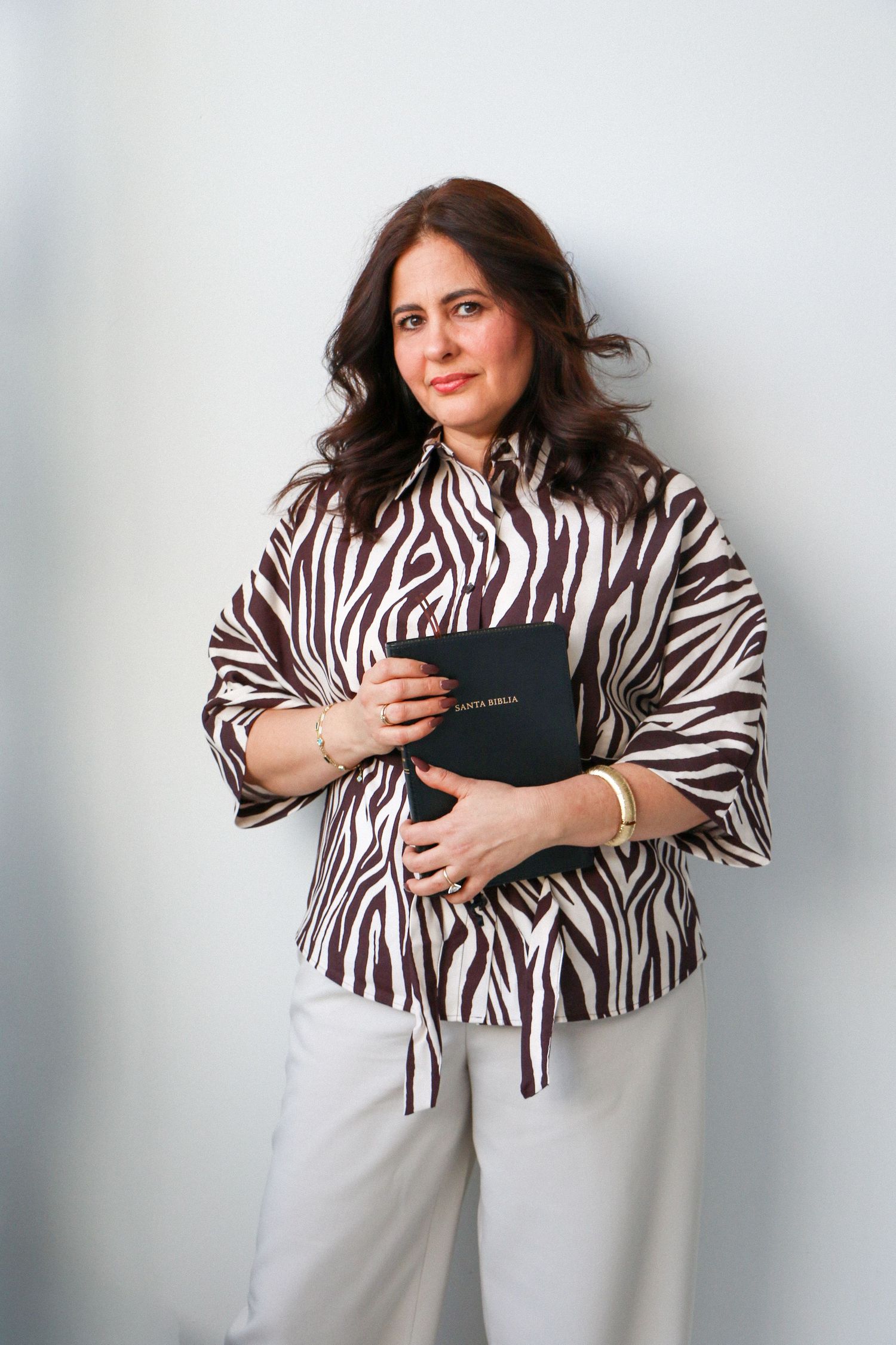 Woman in zebra print shirt holding a Santa Biblia against a light gray background.