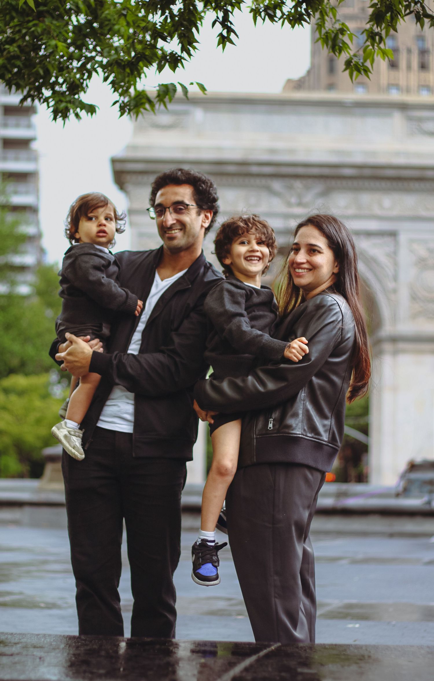 Happy family of four posing in rain near Washington Square Arch in New York City.