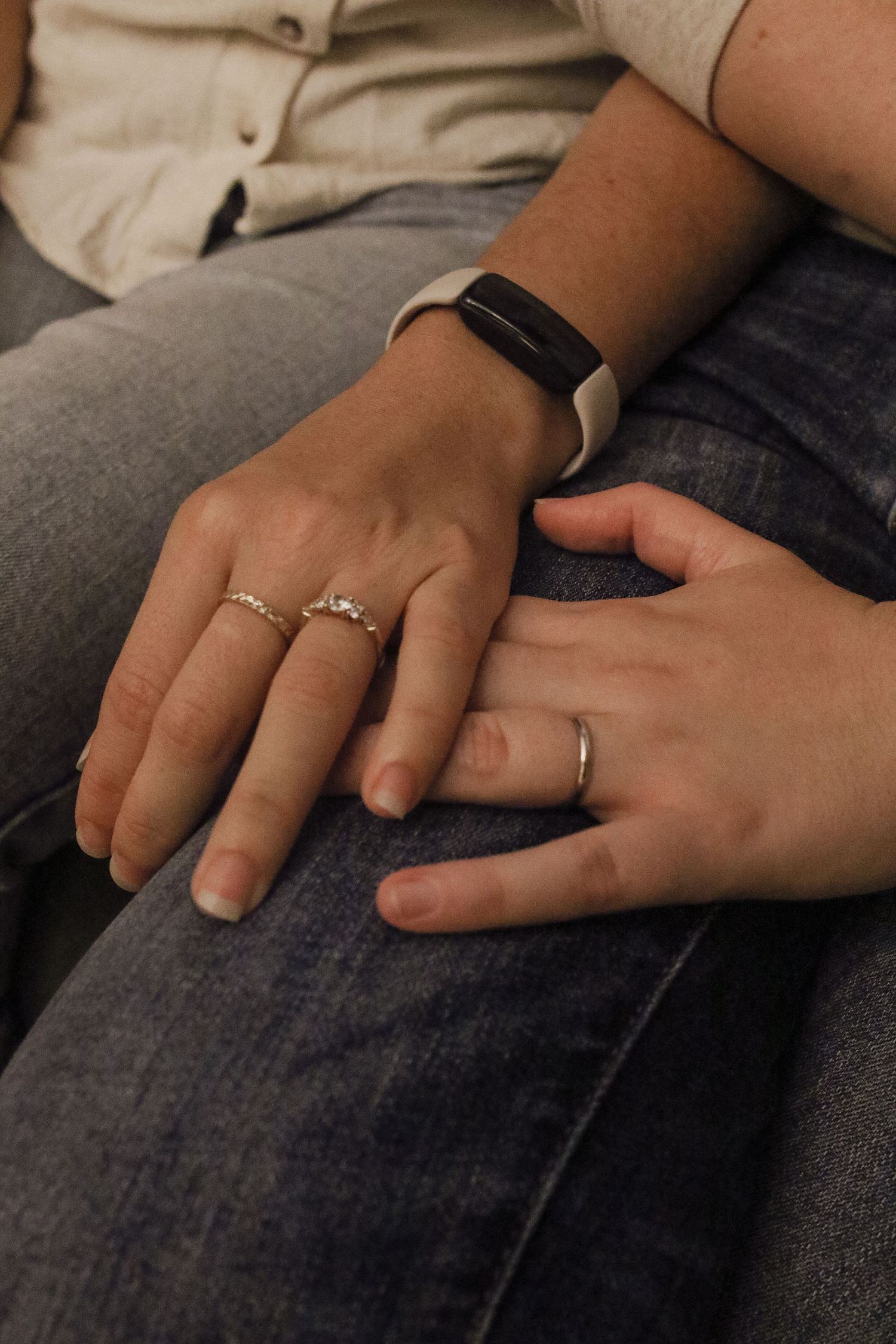 Close-up of two hands with wedding rings touching, one wearing a black fitness tracker bracelet.