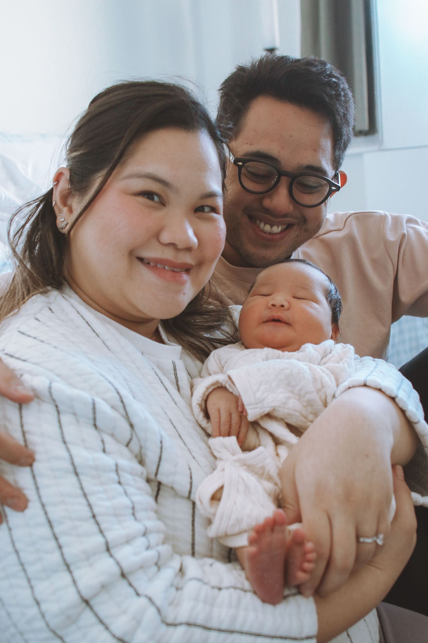 Smiling Asian couple posing with their sleeping newborn baby in white wrap.