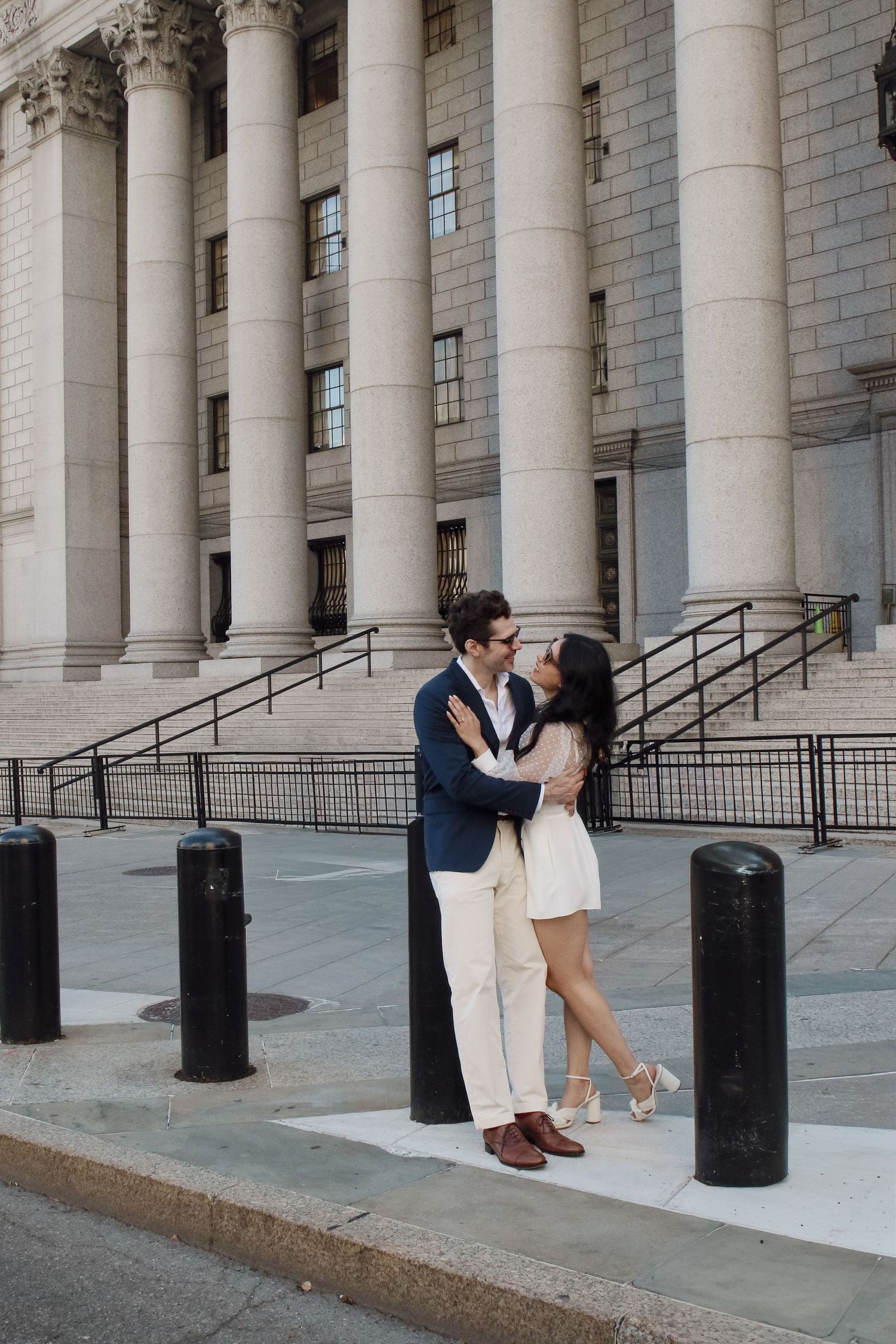 Newlyweds embrace romantically in front of grand neoclassical building columns after their NYC courthouse wedding.