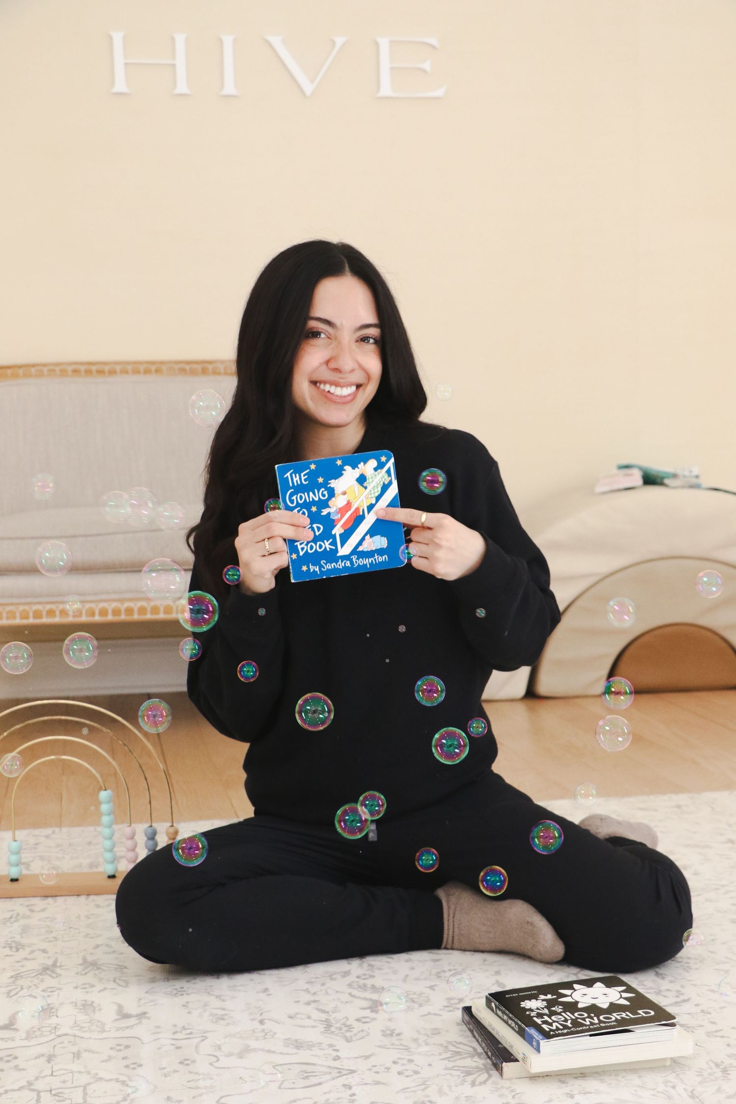 Smiling young woman sitting cross-legged holding a blue children's book with bubbles floating around her.