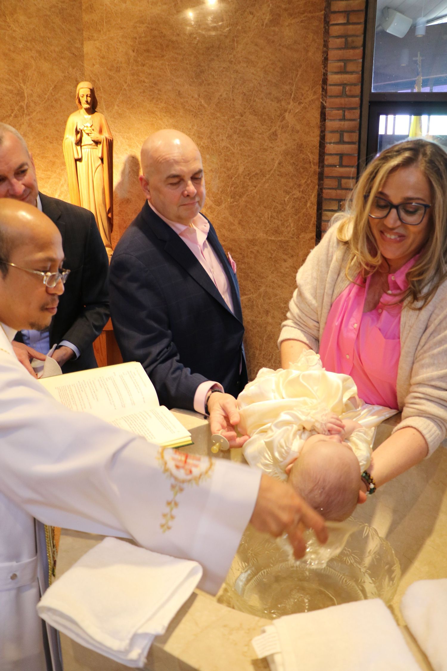 Priest baptizing a baby at a church font during a christening ceremony.