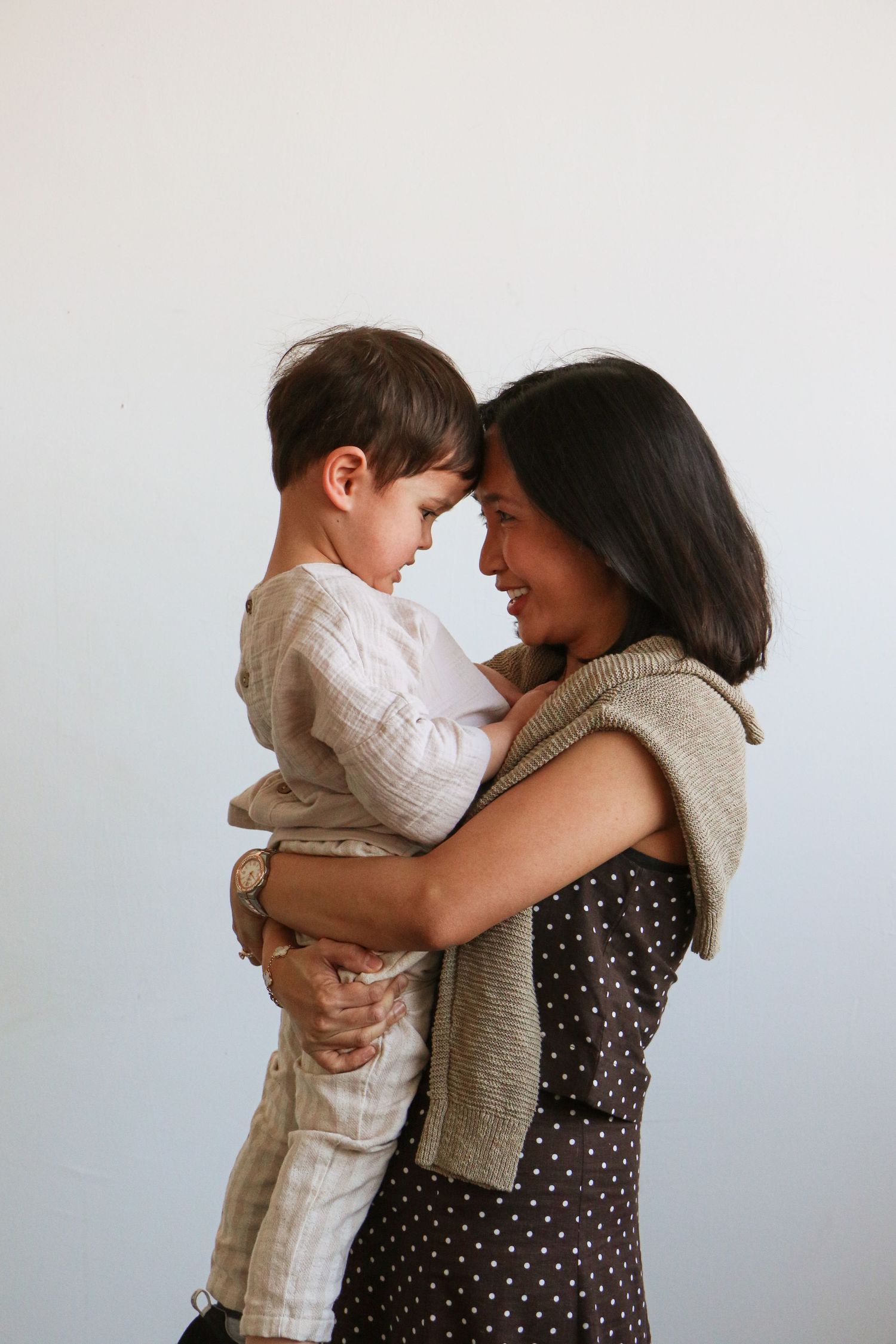 Loving mother holding her young son face-to-face, touching foreheads in a tender moment during a studio portrait.