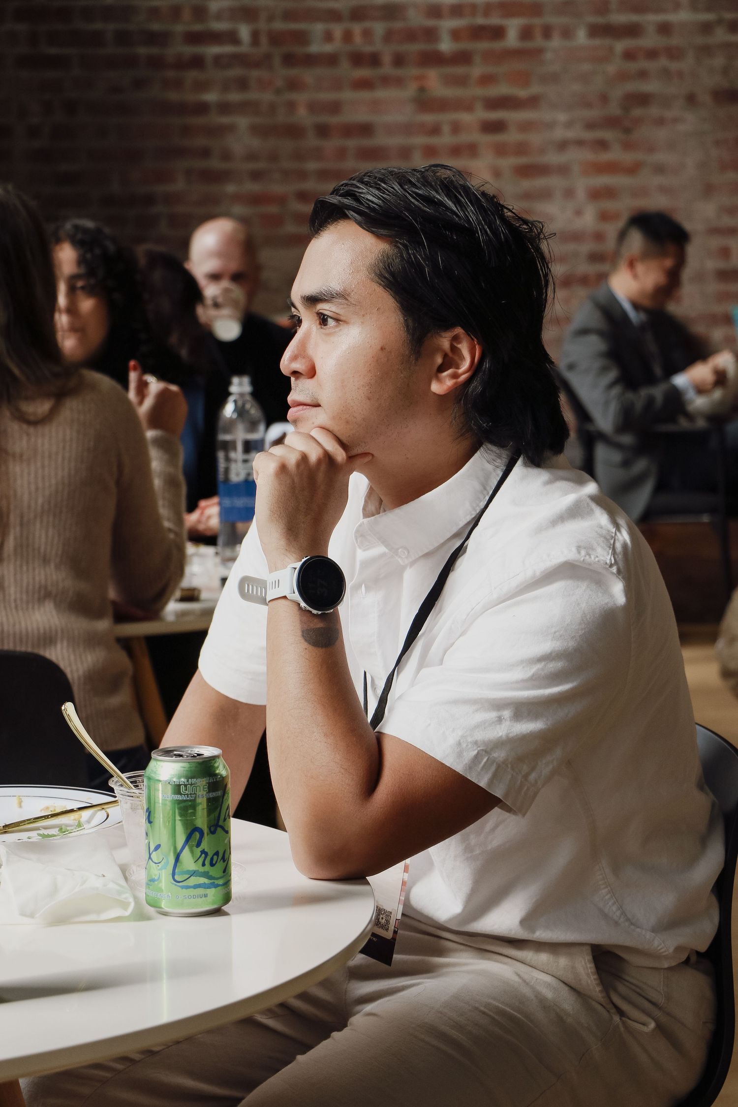 Young Asian man sitting at a white table with a green soda can, resting chin on hand thoughtfully.