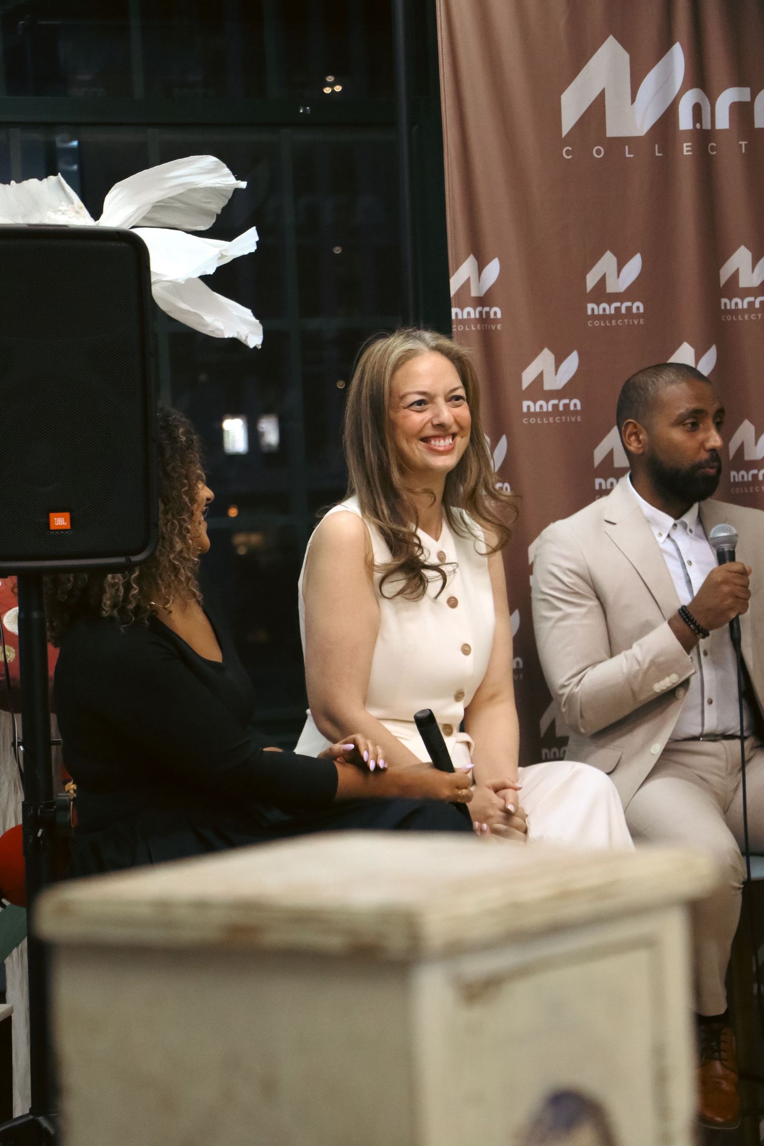 Three people seated on stage at a Norra Collective event, smiling at the audience.