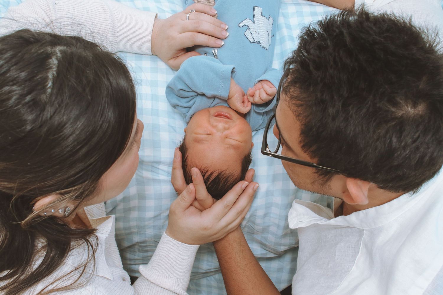 Asian parents looking down lovingly at their newborn baby in blue outfit.