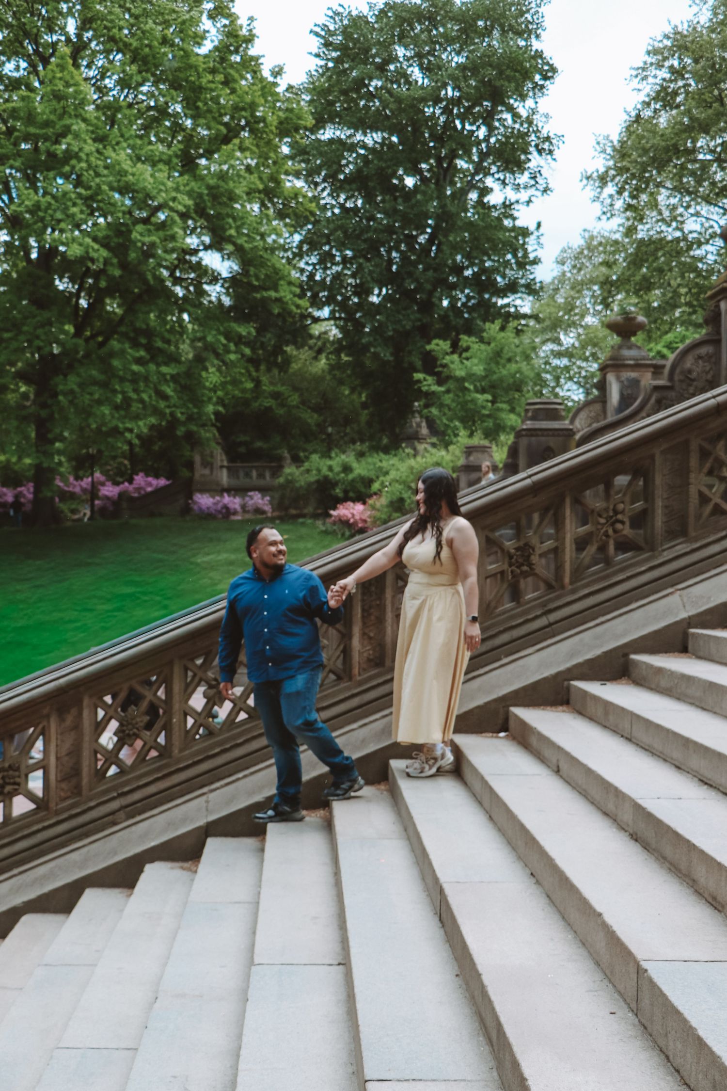Couple holding hands walking up ornate stone stairs at Bethesda Terrace in Central Park, NYC.