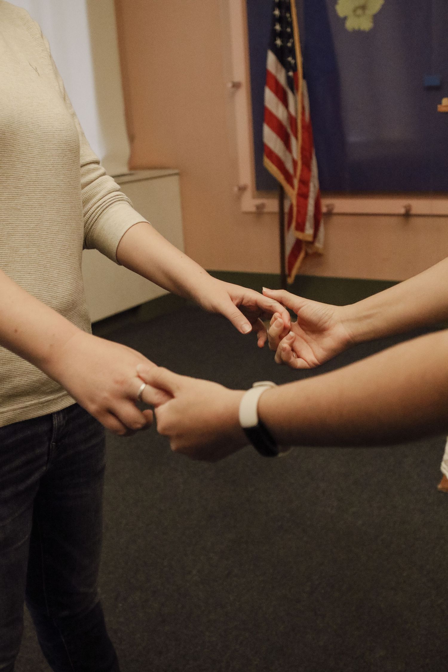 Two people exchanging rings during a civil ceremony with an American flag in the background.