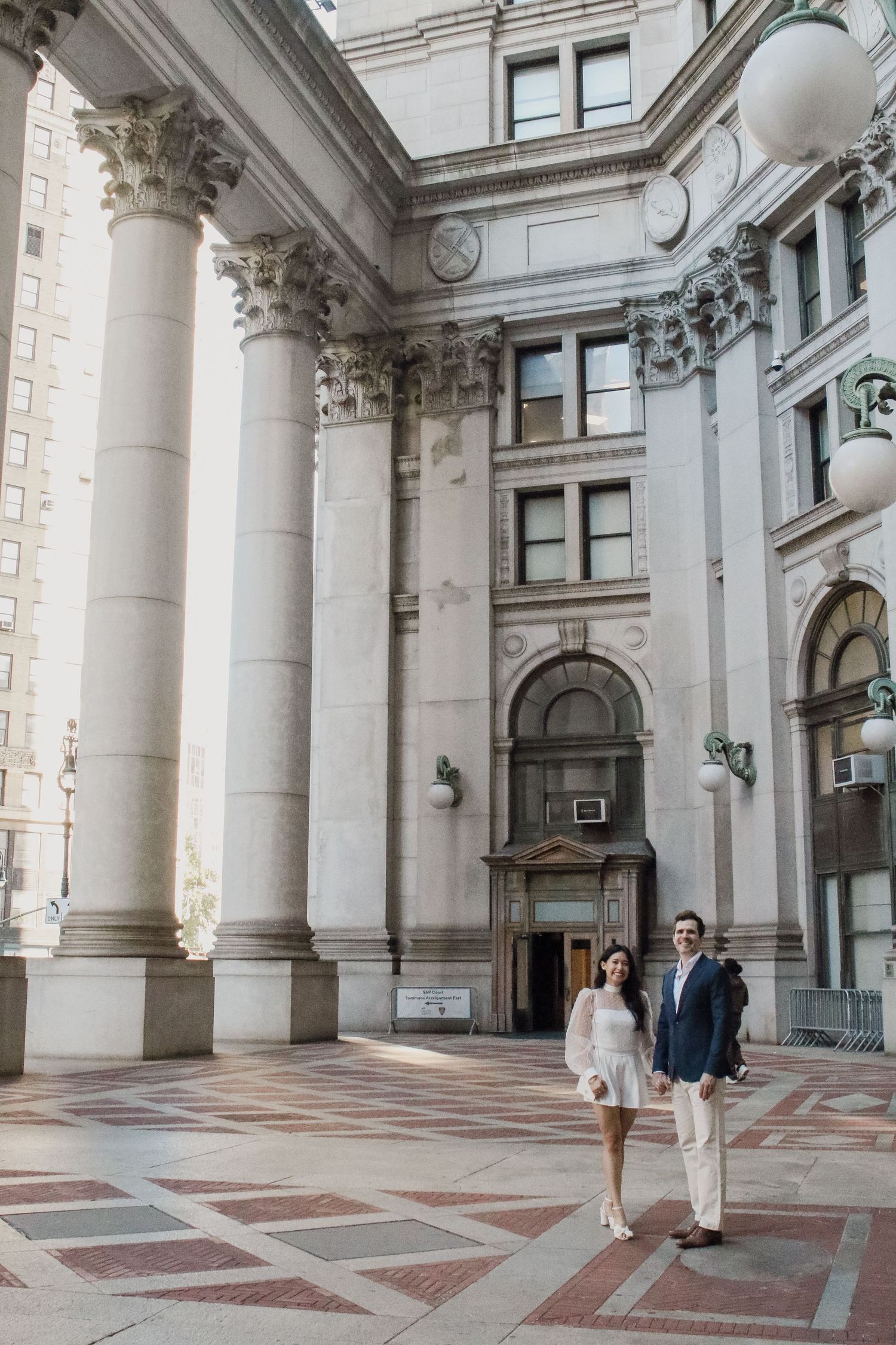 Newlywed couple stands hand in hand in grand courtyard of NYC civic building with towering Corinthian columns.