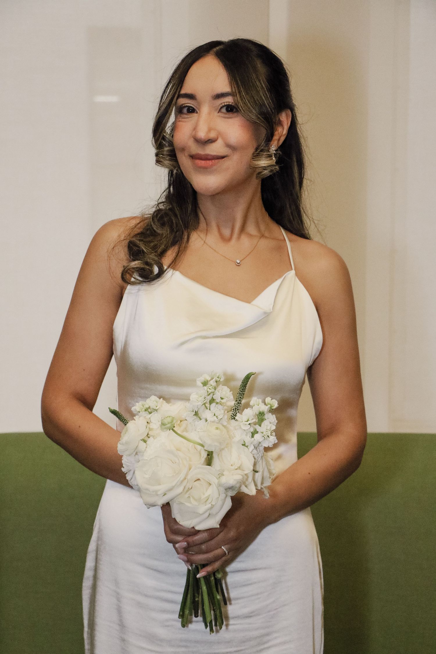 Beautiful bride in white satin halter gown holds white rose bouquet, posing elegantly before her NYC wedding.