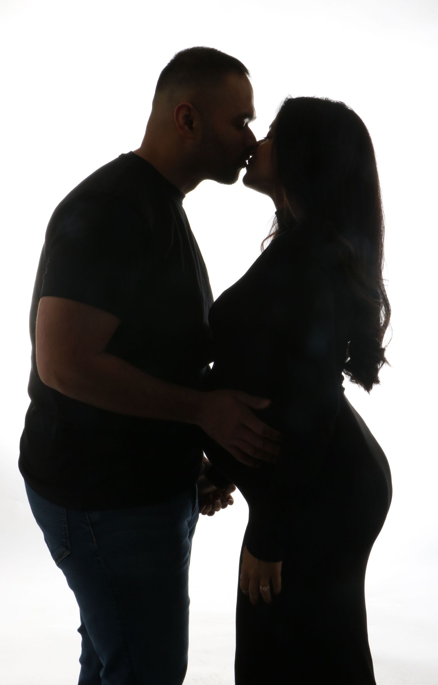 Silhouette of couple kissing while man tenderly holds pregnant partners baby bump.