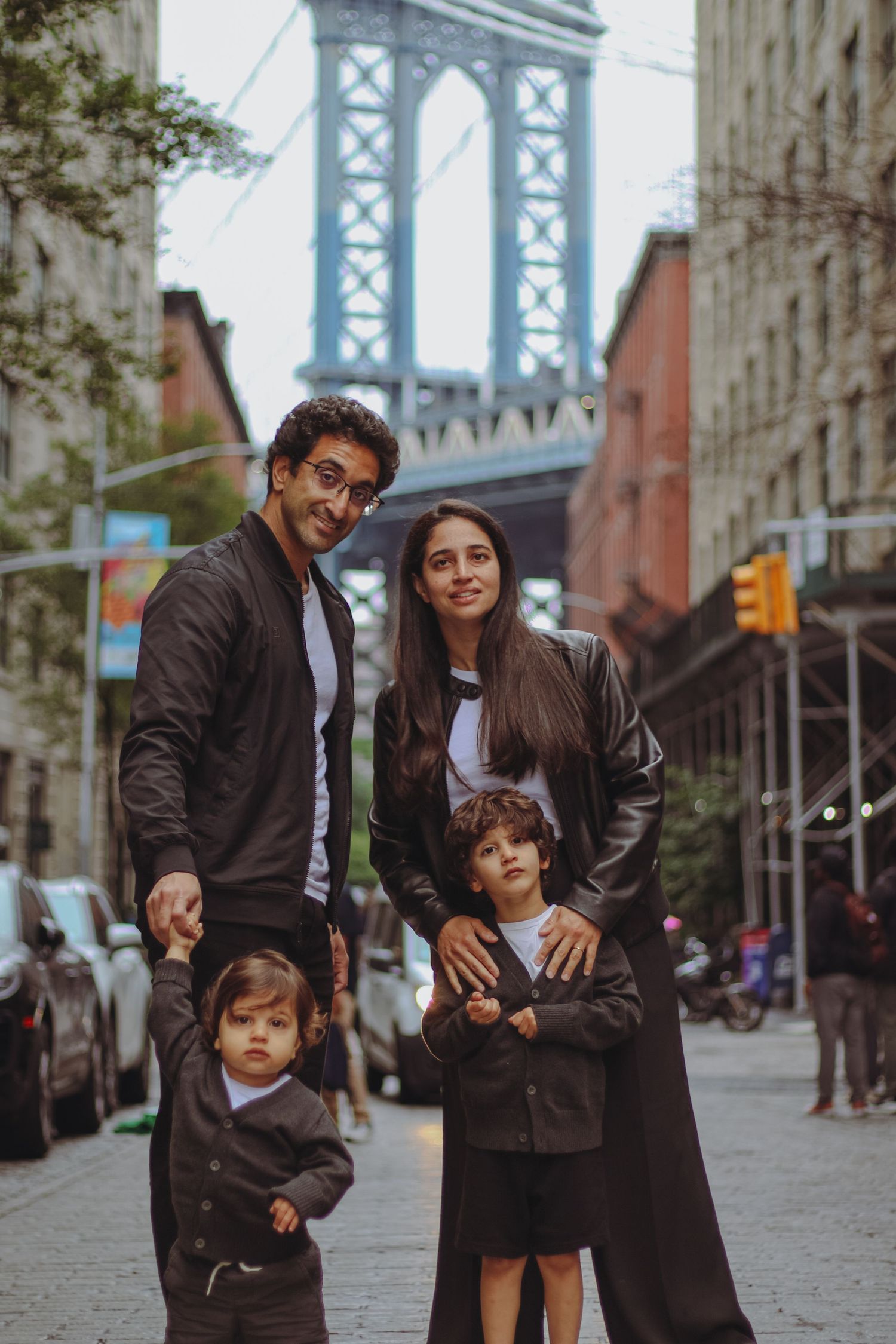 Family of four smiling together on a cobblestone street with Manhattan Bridge in background.