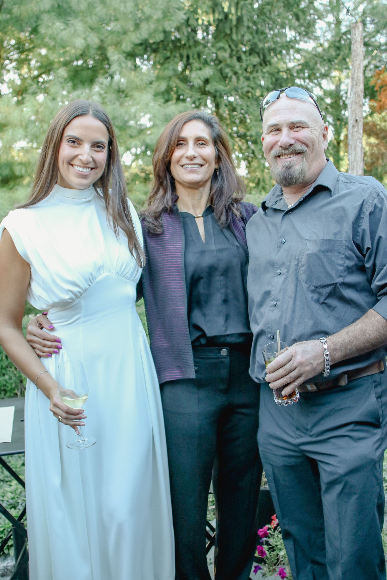 Three adults smiling together outdoors at garden party event.