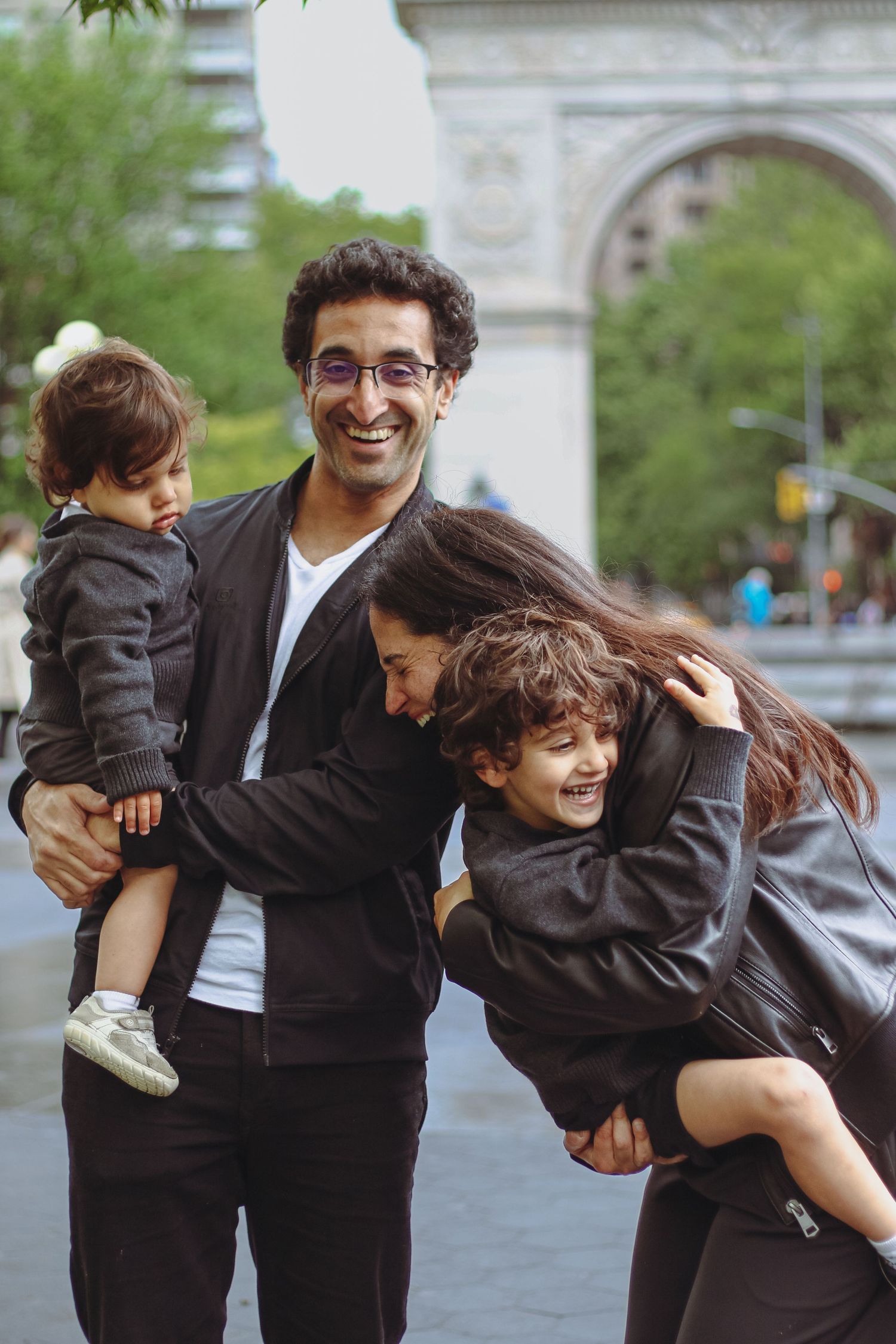 Happy family of four laughing and hugging near Washington Square Arch in New York City.