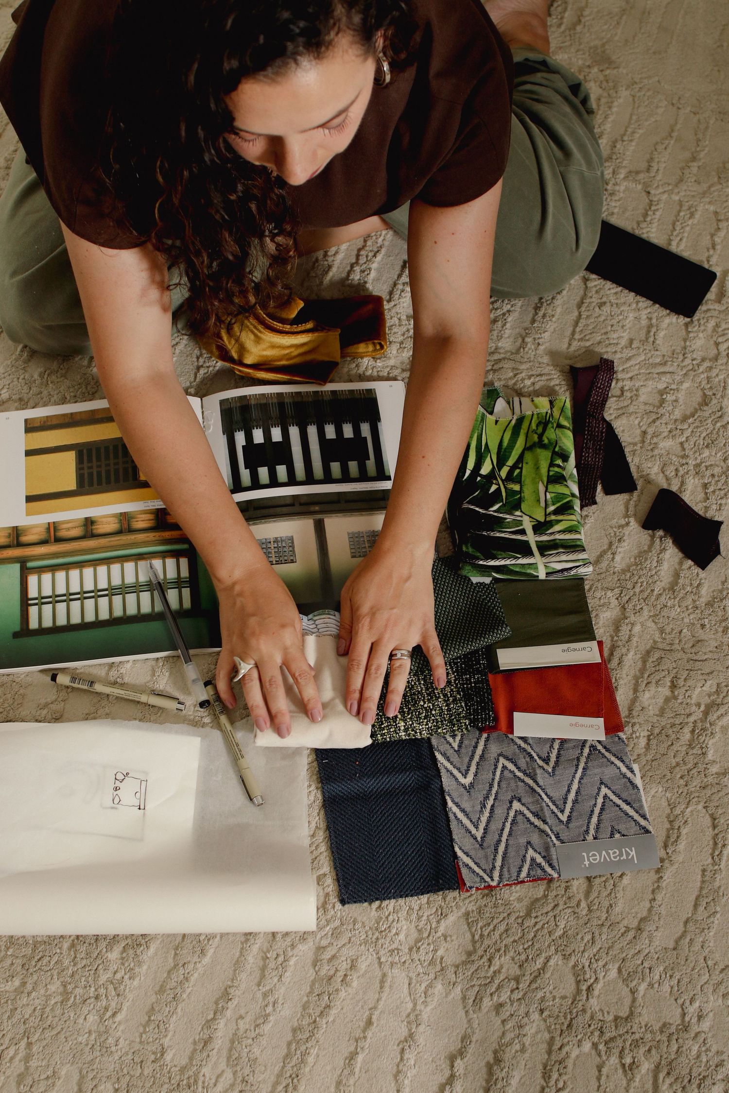 Overhead view of woman arranging fabric swatches and design samples on floor for interior design.