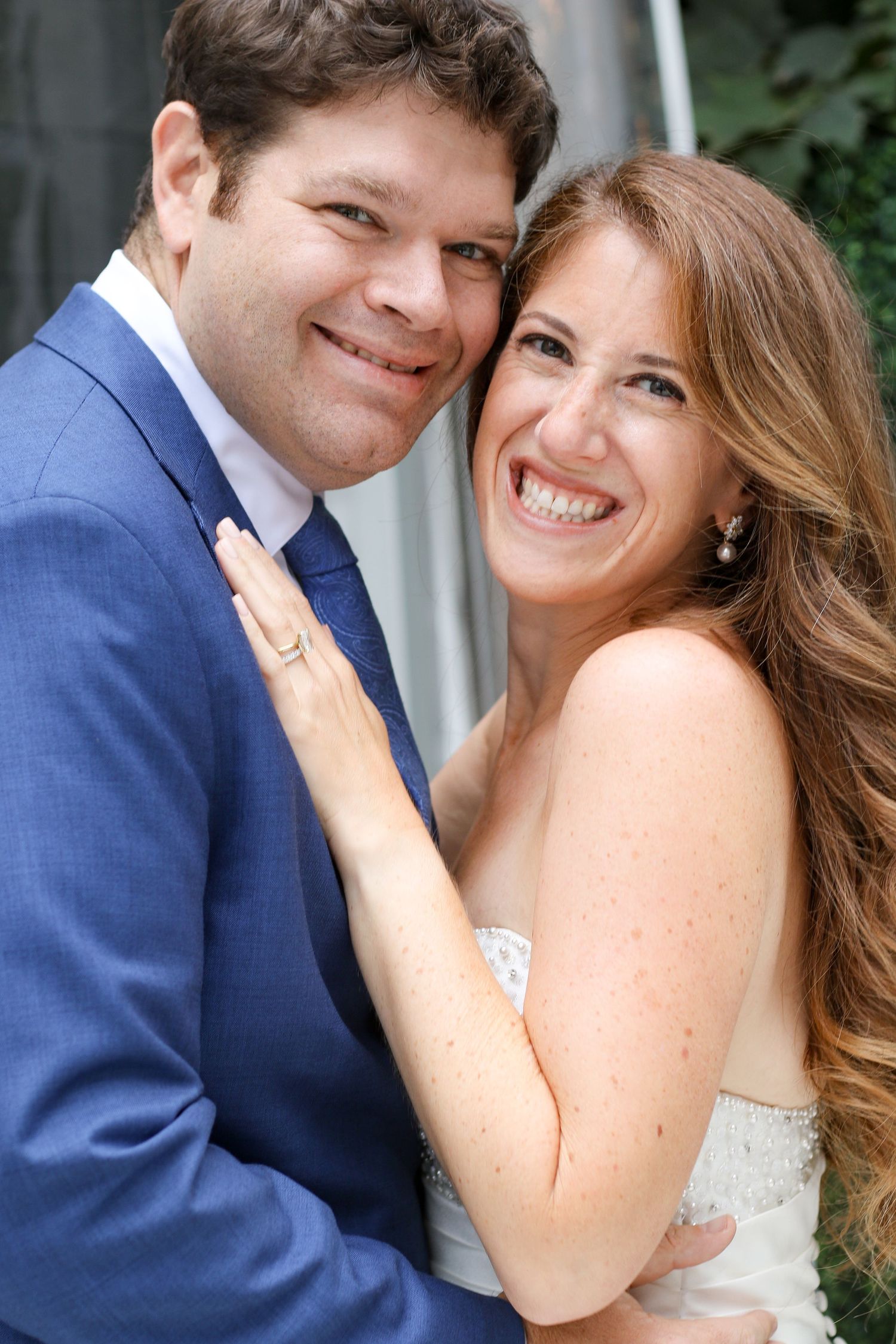 Smiling bride and groom in blue suit share a joyful close portrait at their outdoor wedding.