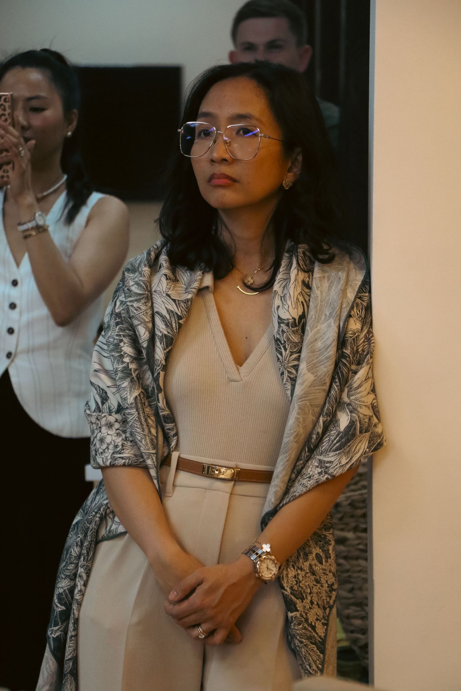 Elegant woman in patterned kimono jacket and glasses standing at indoor event.