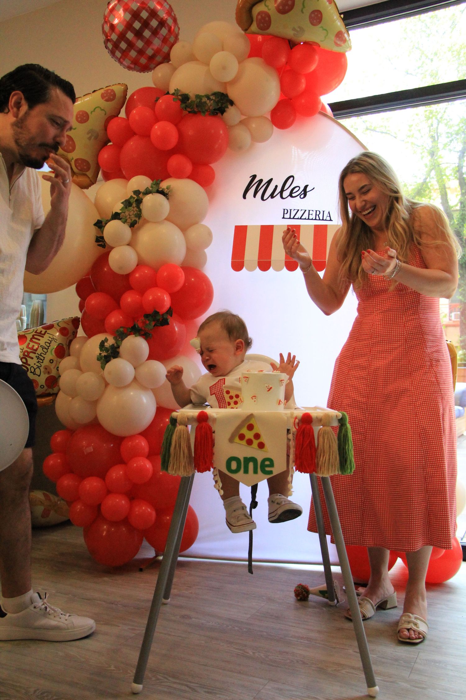 Parents celebrate with their baby at Miles Pizzeria themed first birthday party with balloon arch.