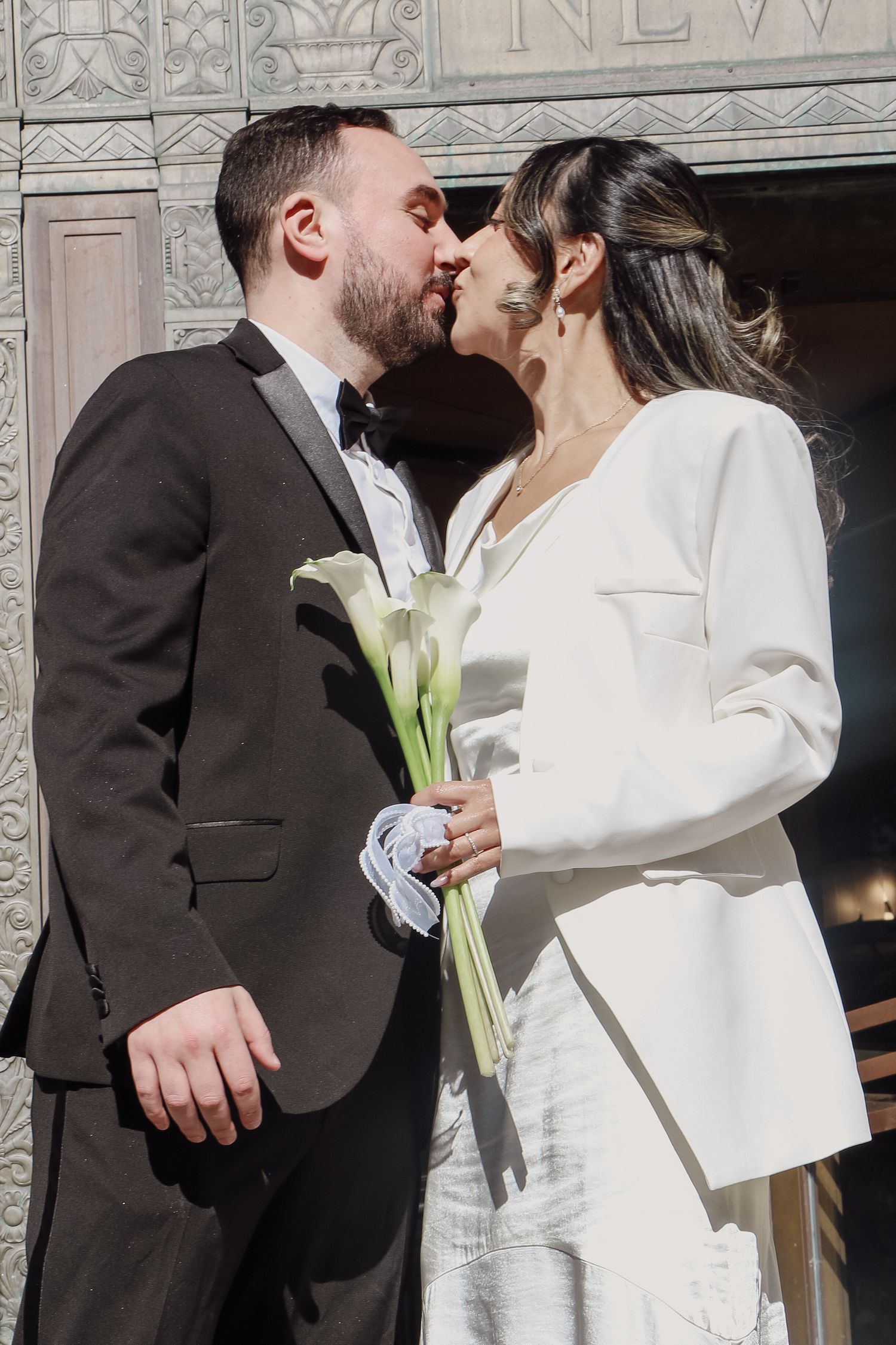 Newlyweds share a kiss outside NYC City Clerk office, bride holding white calla lily bouquet.