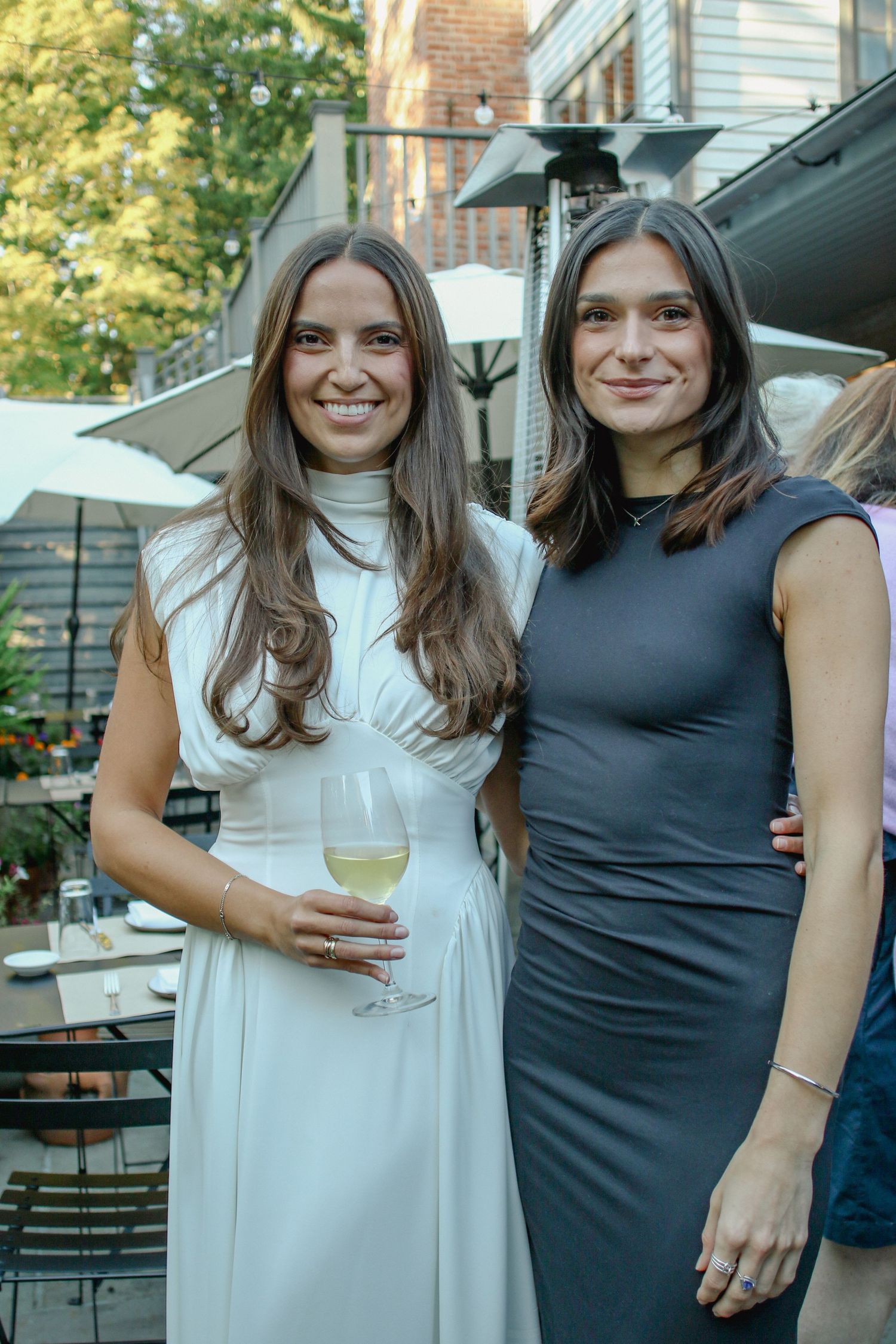 Two young women in elegant dresses smiling at outdoor garden party.