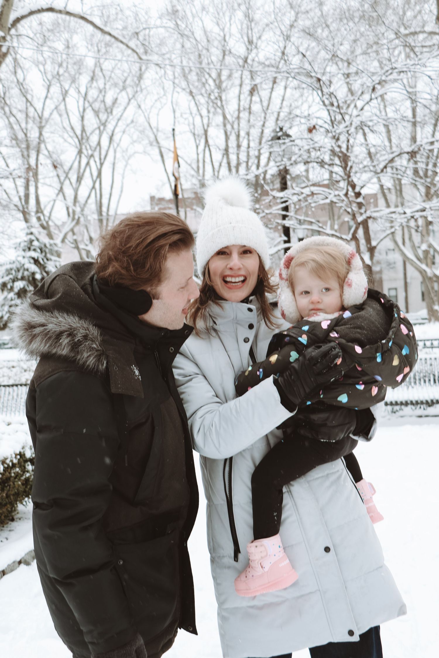 Smiling family with a toddler enjoying a snowy day in a winter park.