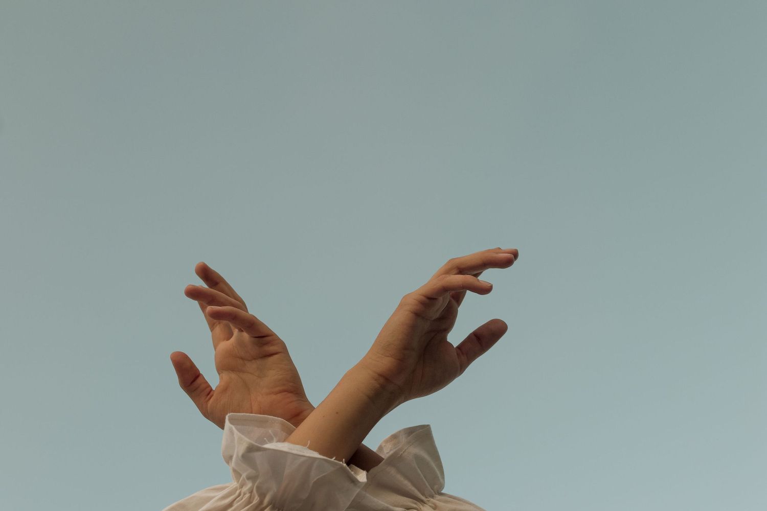 photo of hands lifted into sky, arms covered in long flowing white sleeves