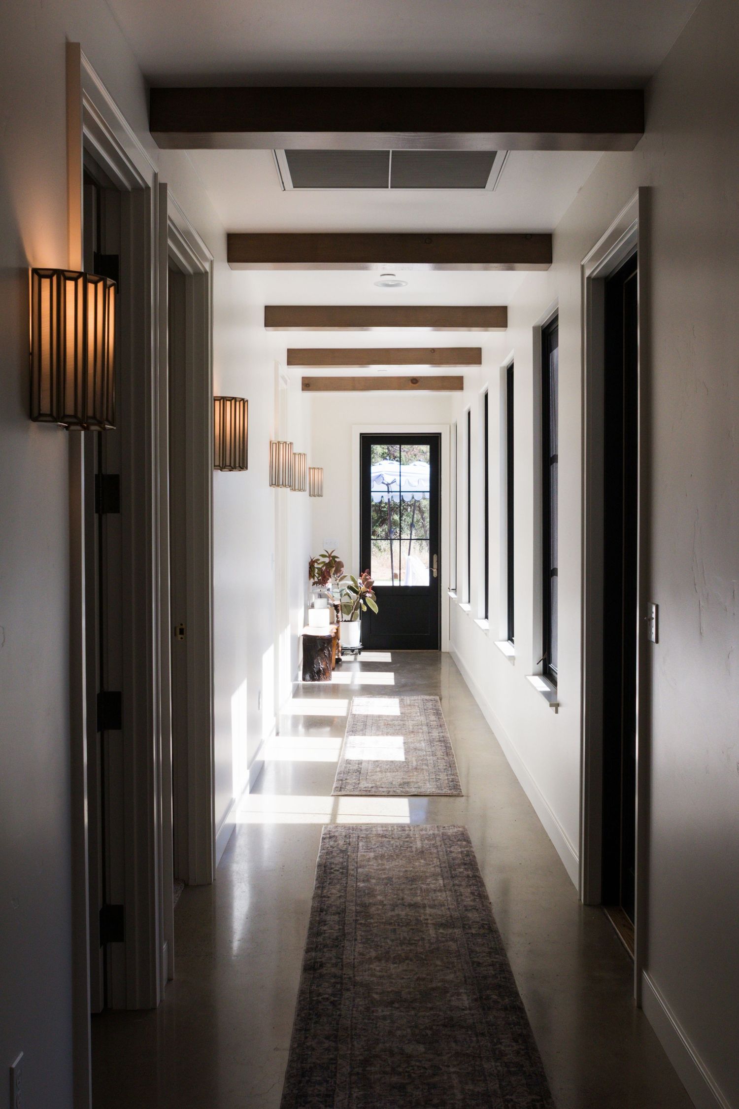 long hallway with beams along ceiling and light fixtures along one wall. windows let in light on the floor
