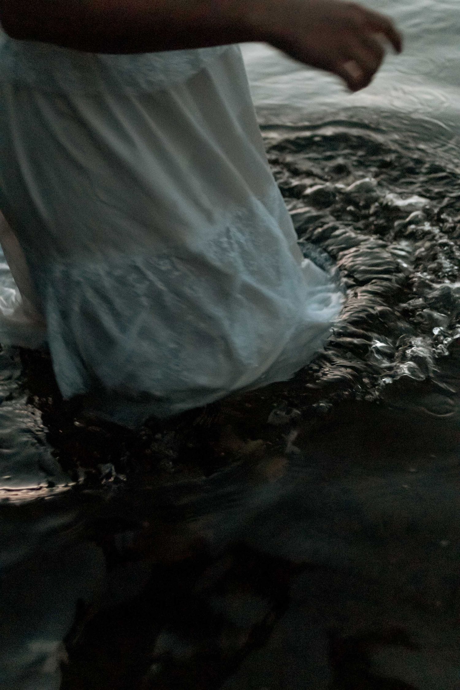 close up of person in white dress wading in water at twilight