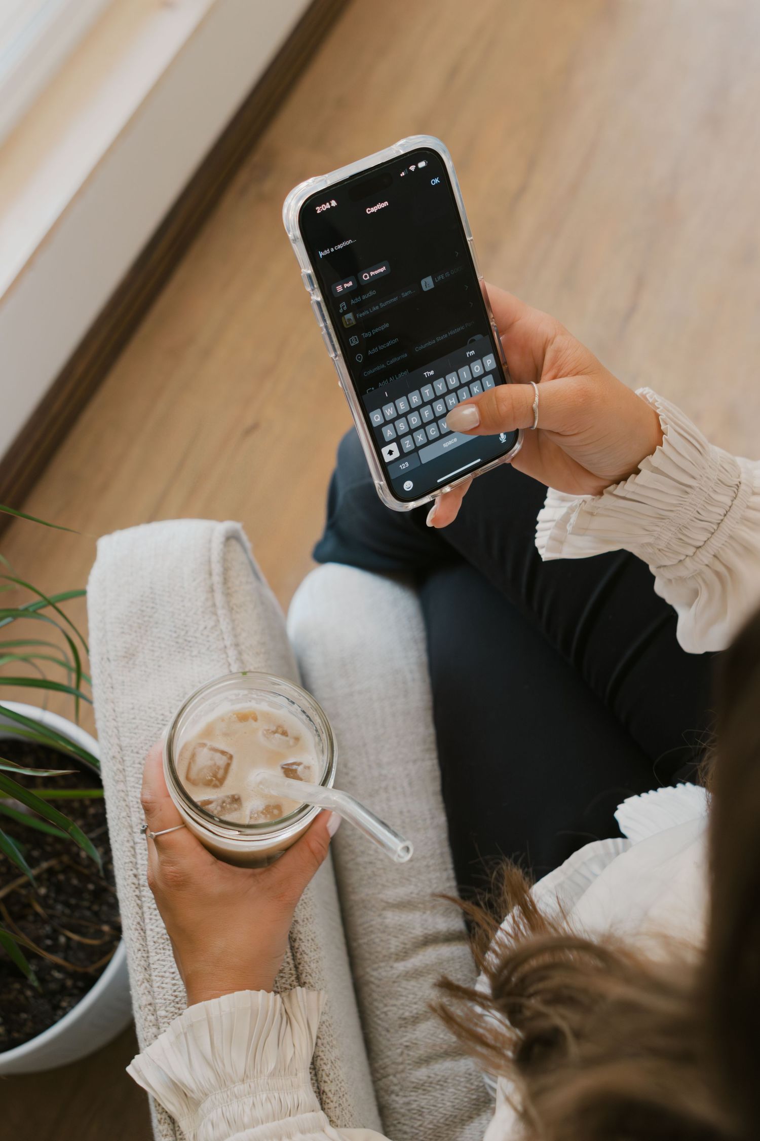 overhead view of woman creating social media post and holding iced latte in other hand