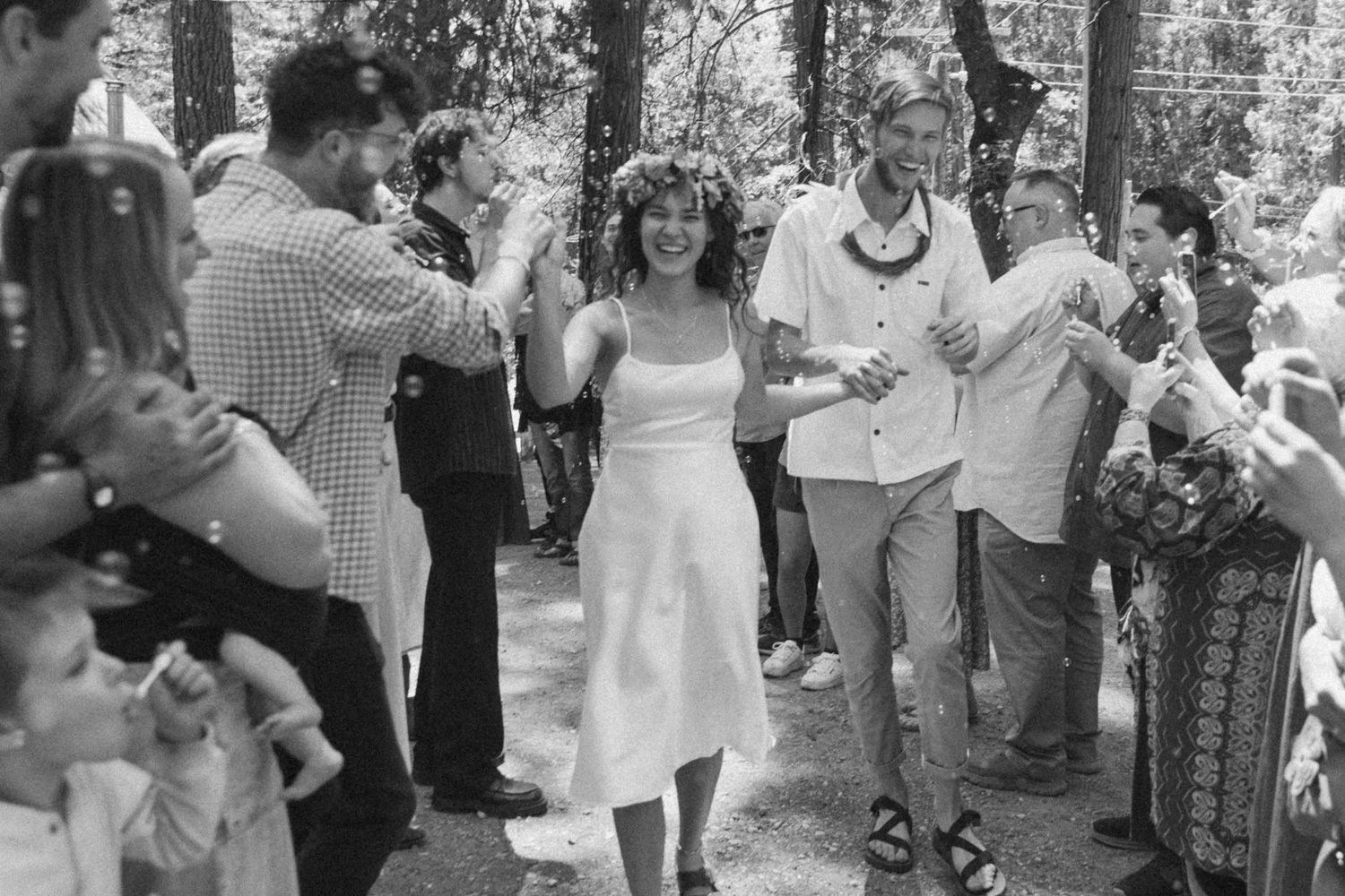 b+w photo of bride and groom leaving reception through crowd of people. bubbles are floating in air