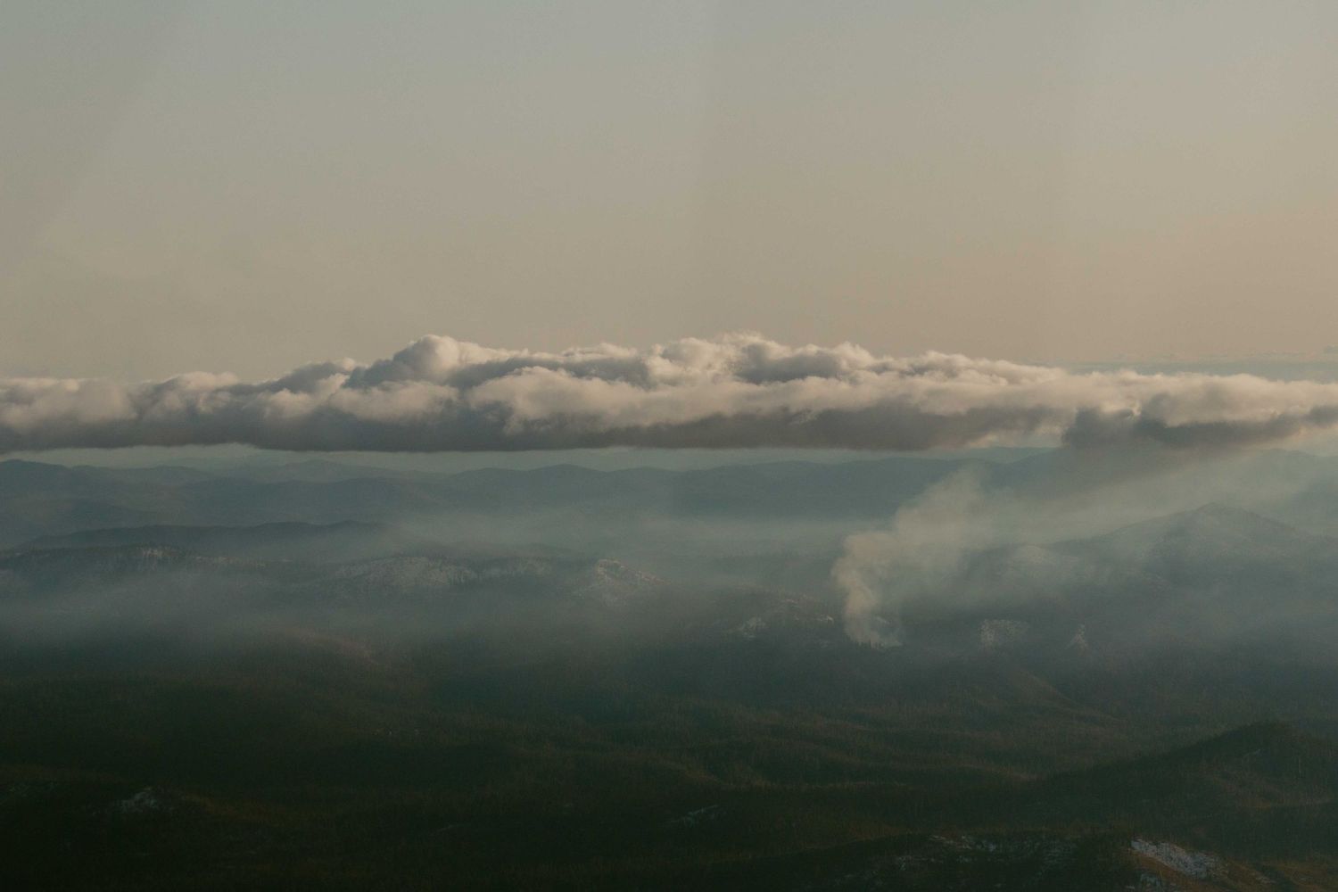 one long skinny cloud sits in light blue sky. wispy clouds cover mountains below
