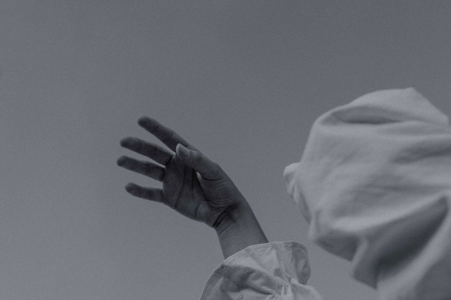 b+w photo of hands lifted into sky, arms covered in long flowing white sleeves