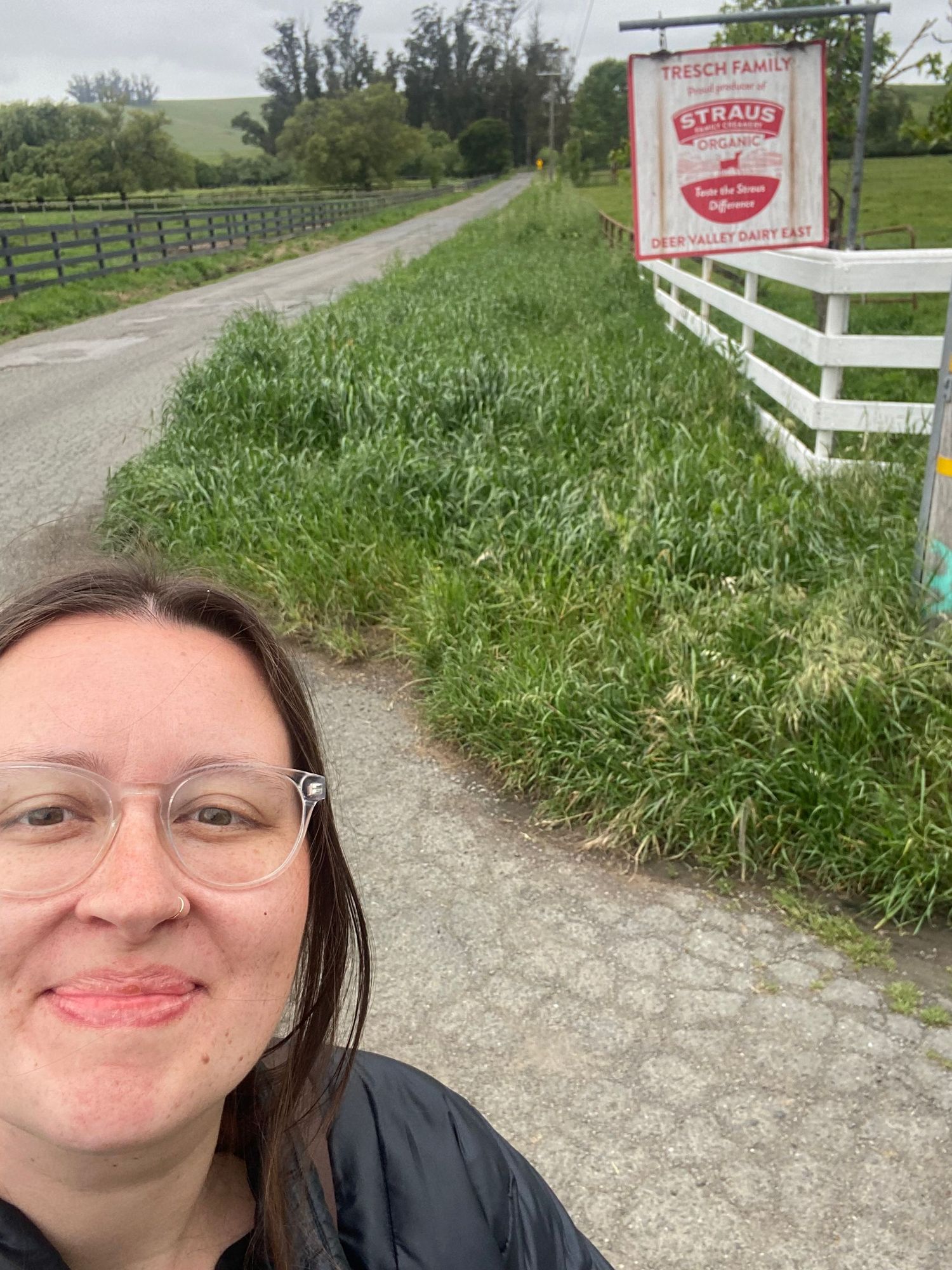 girl wearing glasses standing in front of straus milk farm sign