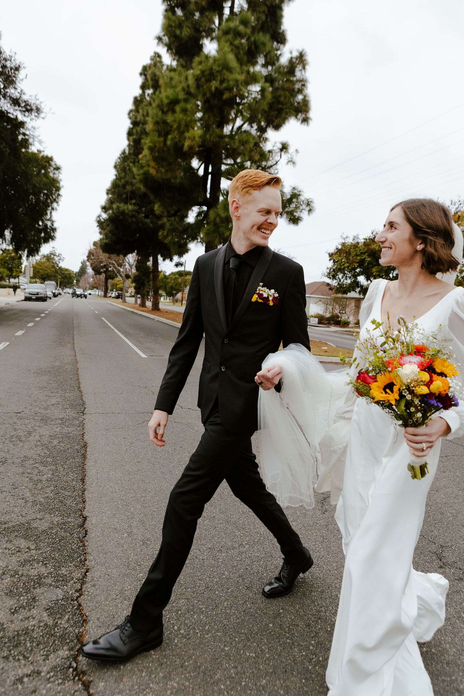 Bride and groom walking across city street. brides carries colorful wildflower bouqet