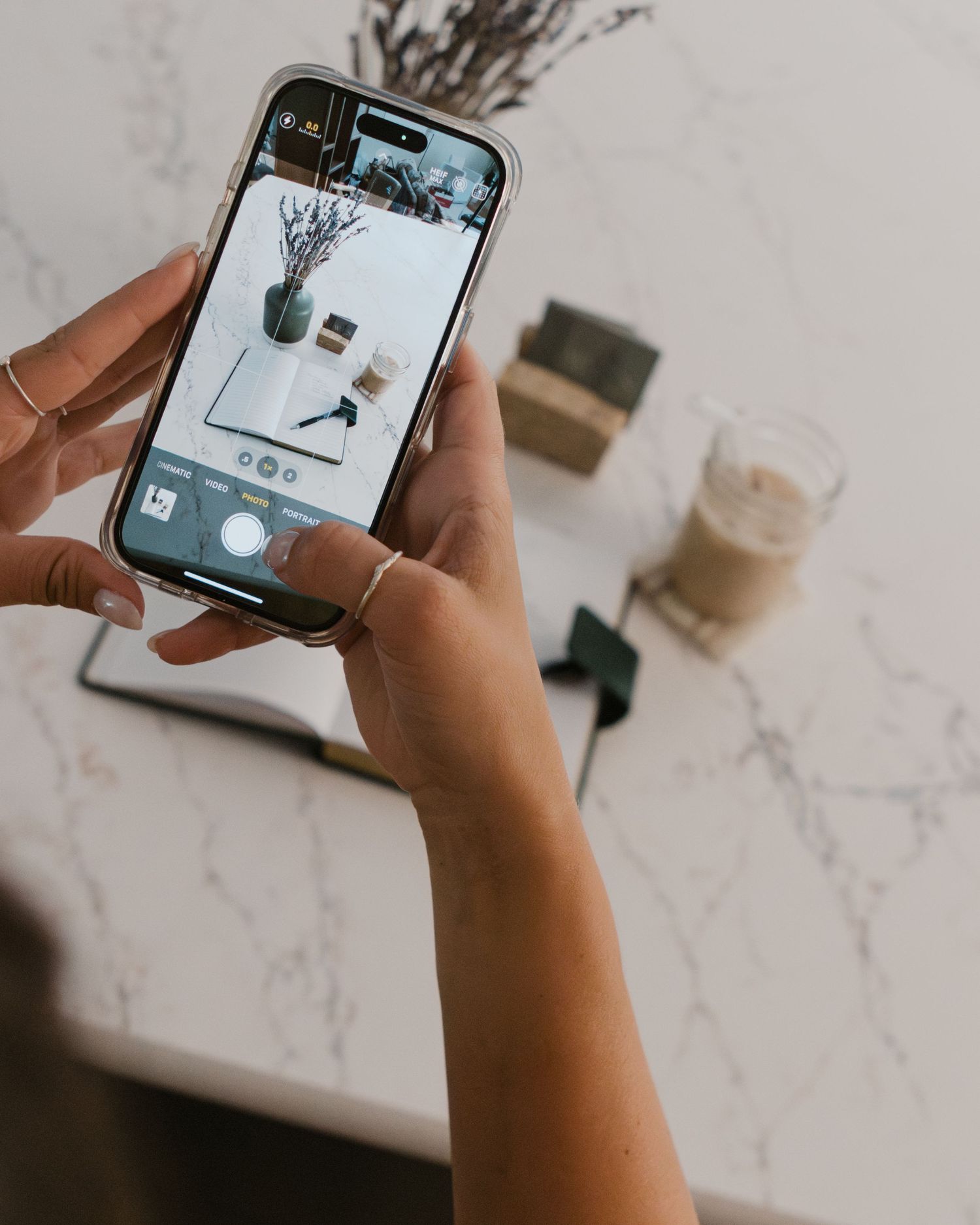 person takes photo with phone of journal and coffee on marble countertop