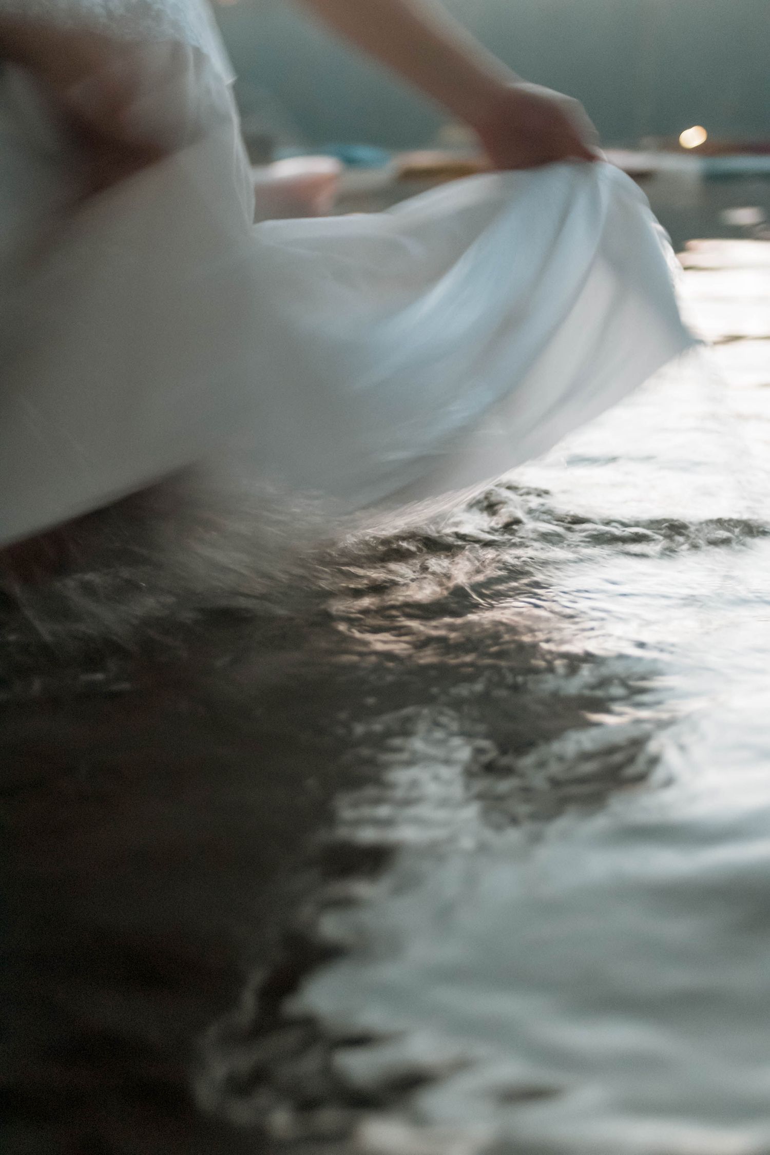 close up of person in white dress wading in water at twilight