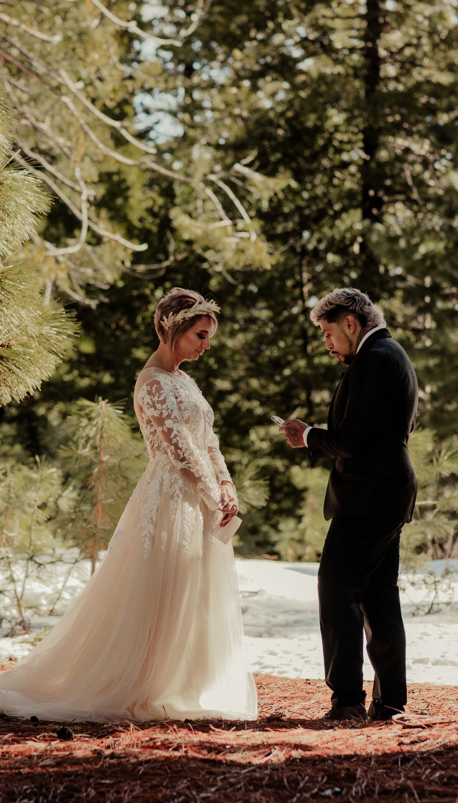 bride and groom say vows below pines with snow surrounding them